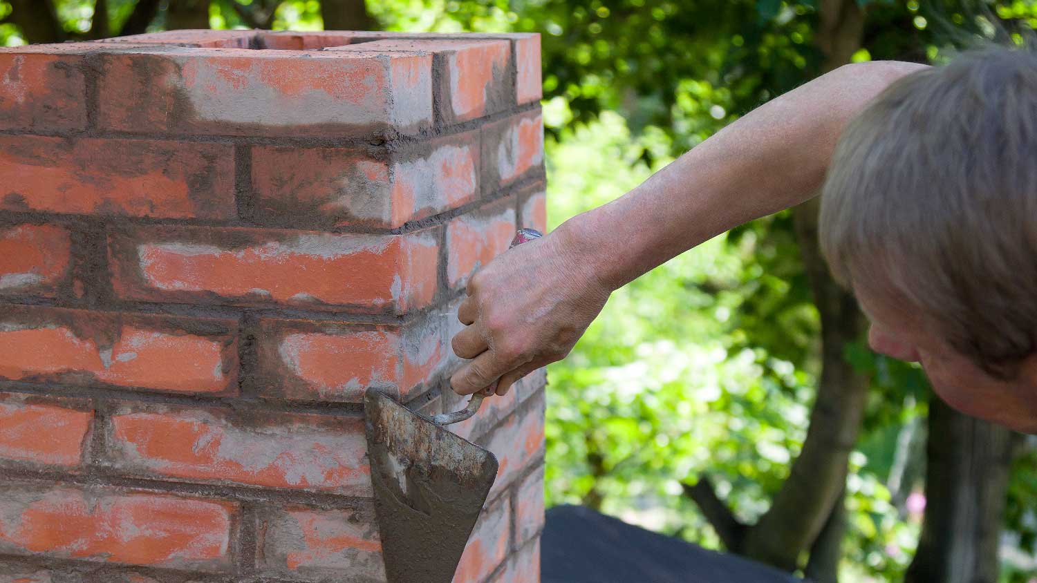 A person tuckpointing a brick chimney