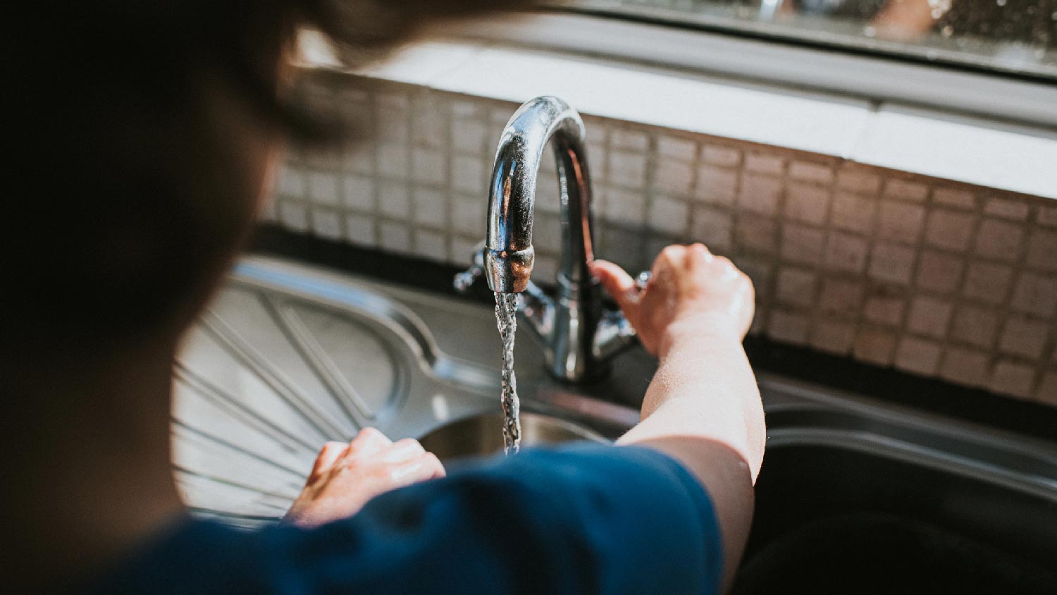 A person turning on a tap of a double-handle faucet