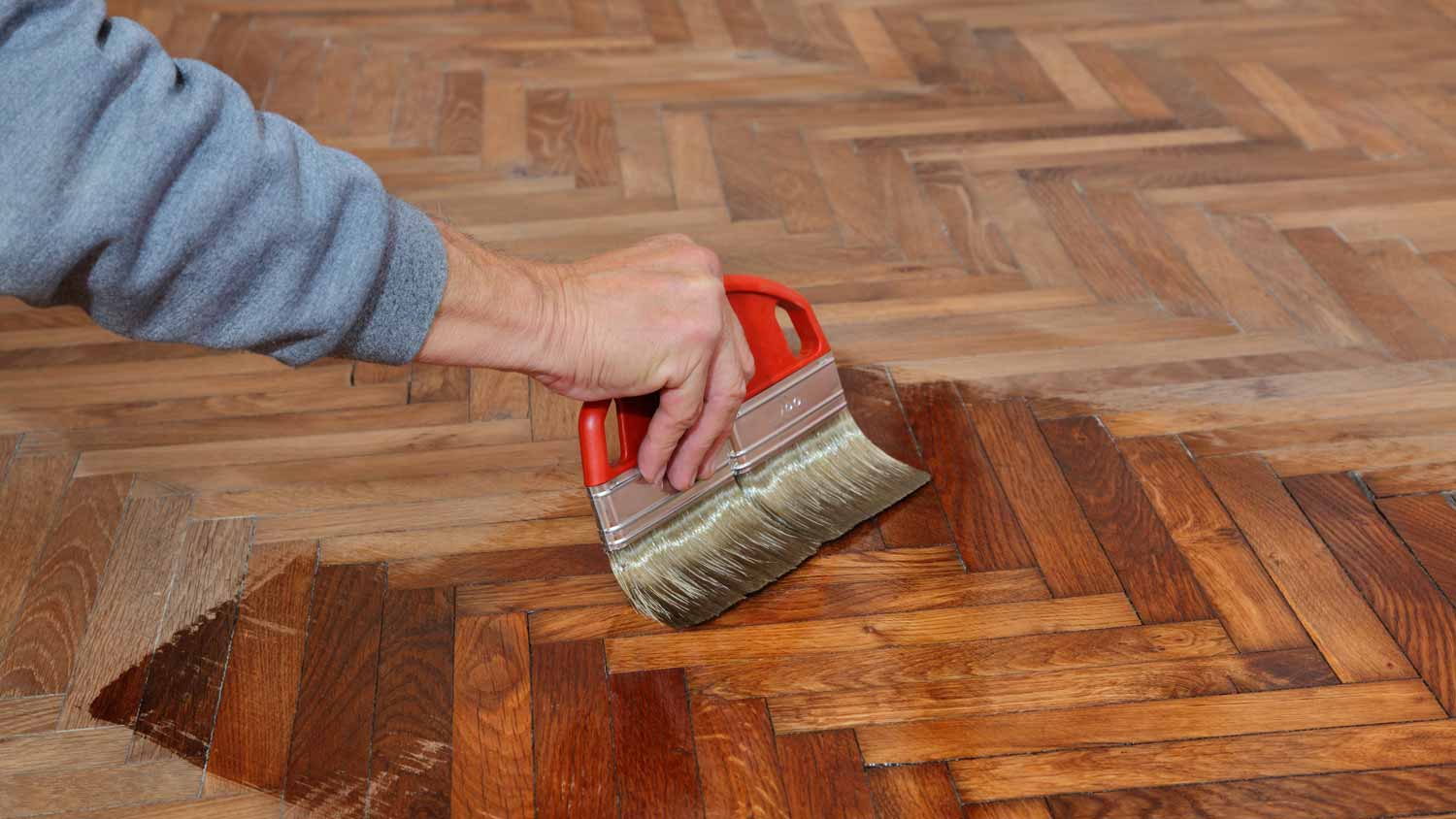 A person varnishing hardwood floor with a brush