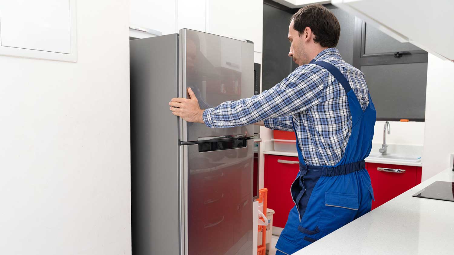 Technician placing new refrigerator in a small kitchen