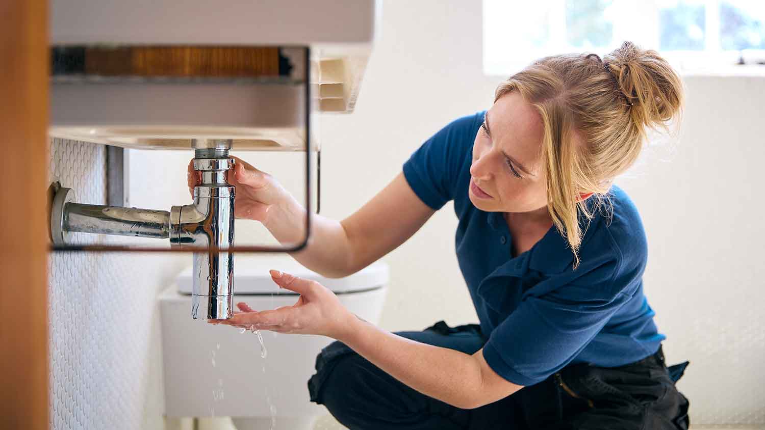 Female plumber fixing bathroom sink pipe