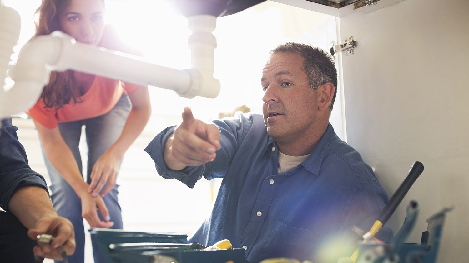 plumber working on pipes under kitchen sink 