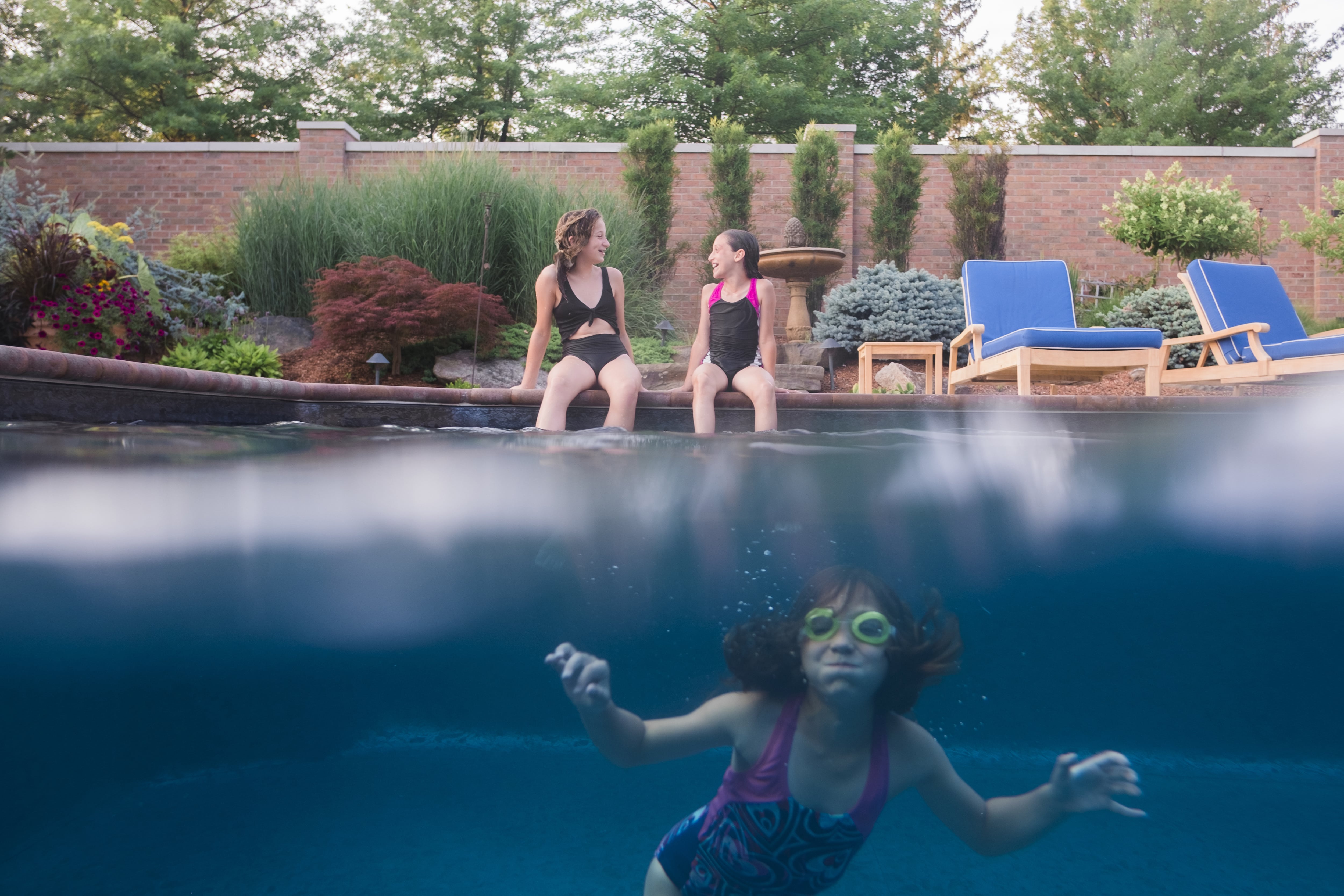 Girl swims while friends chat on the pool side with a brick fence in background