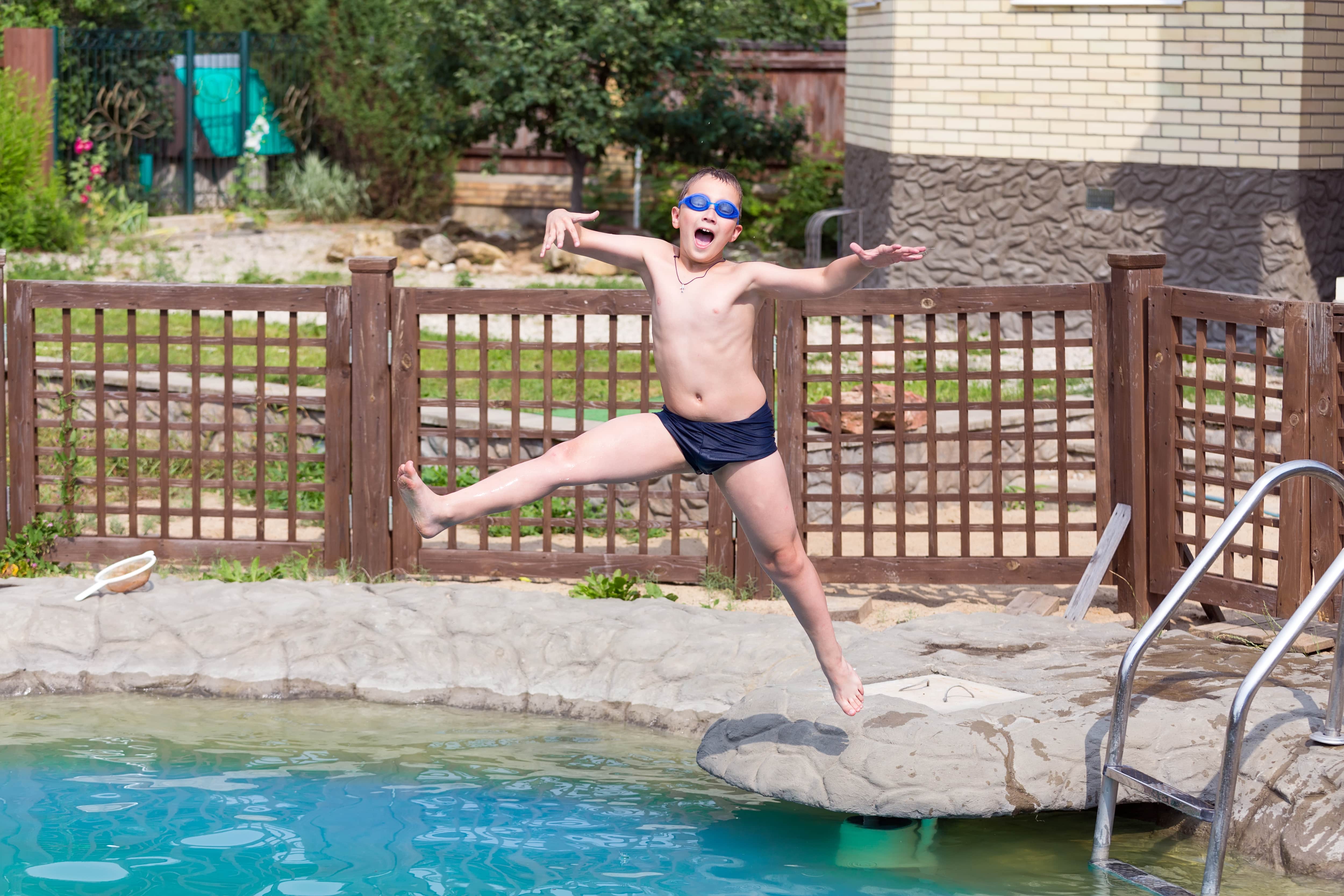 A checkerboard fence encloses a pool while a boy jumps into it