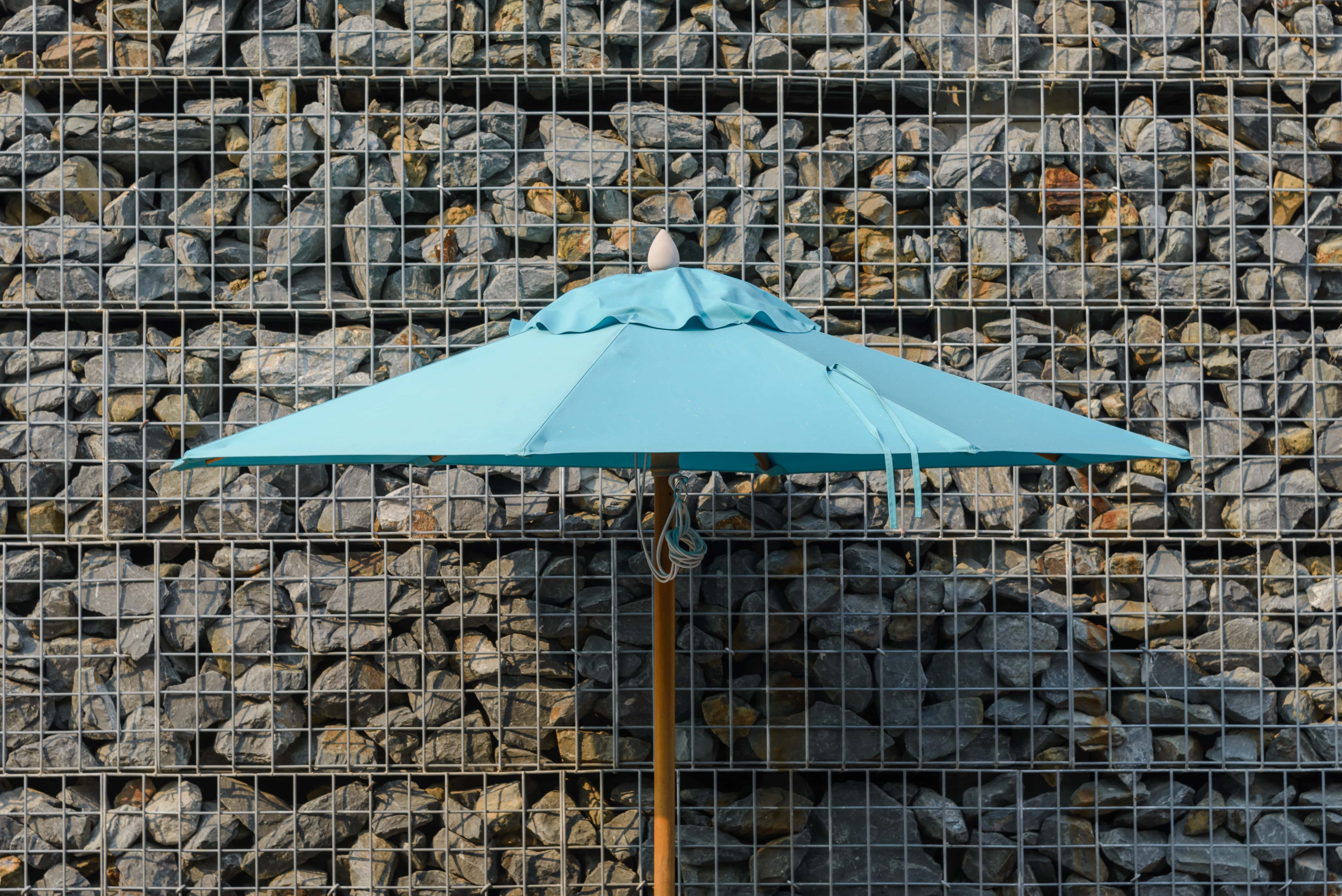 An outdoor umbrella in front of a gabion wall