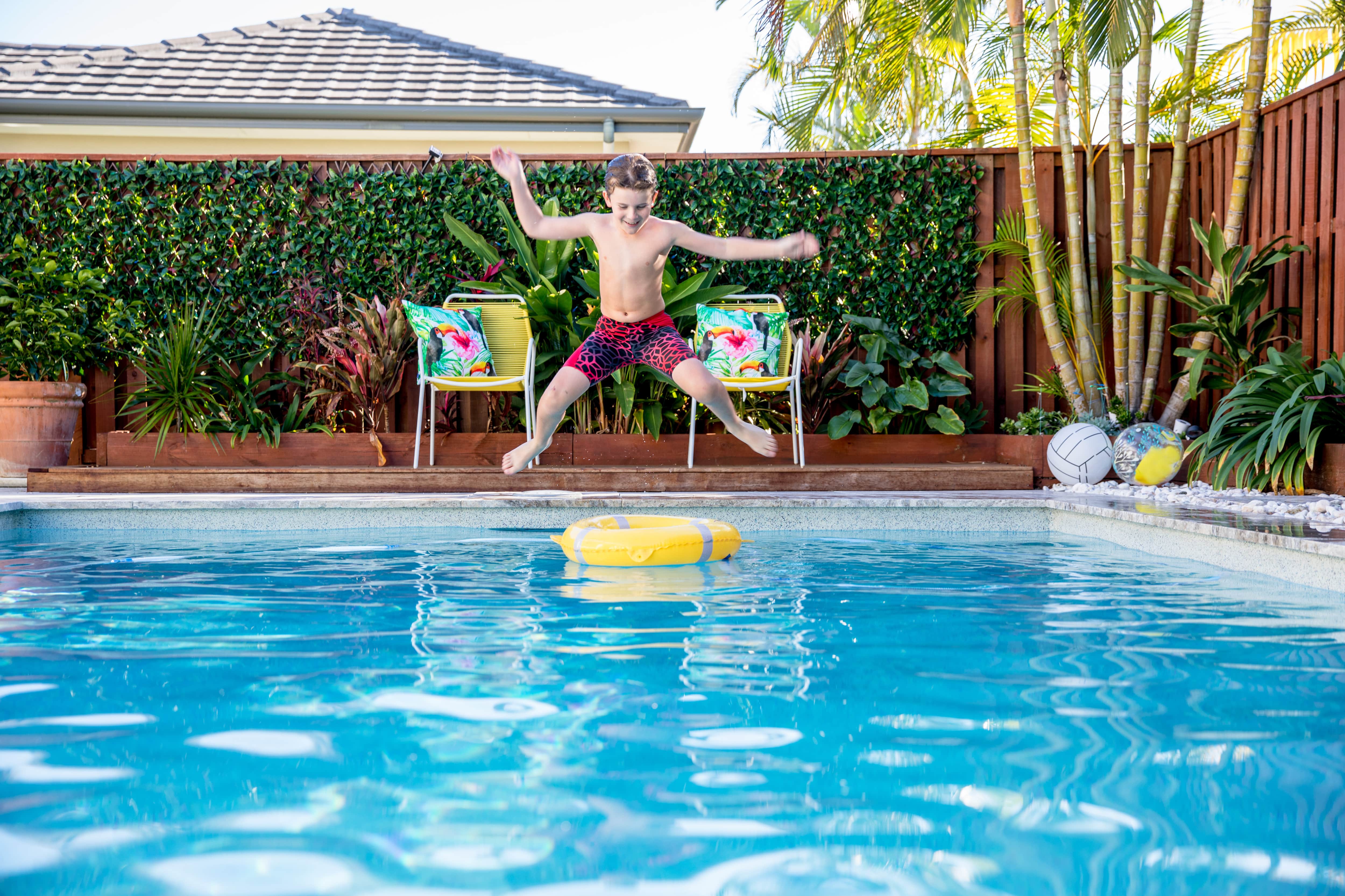 A boy jumps into a pool in front of a wall with vines growing on it