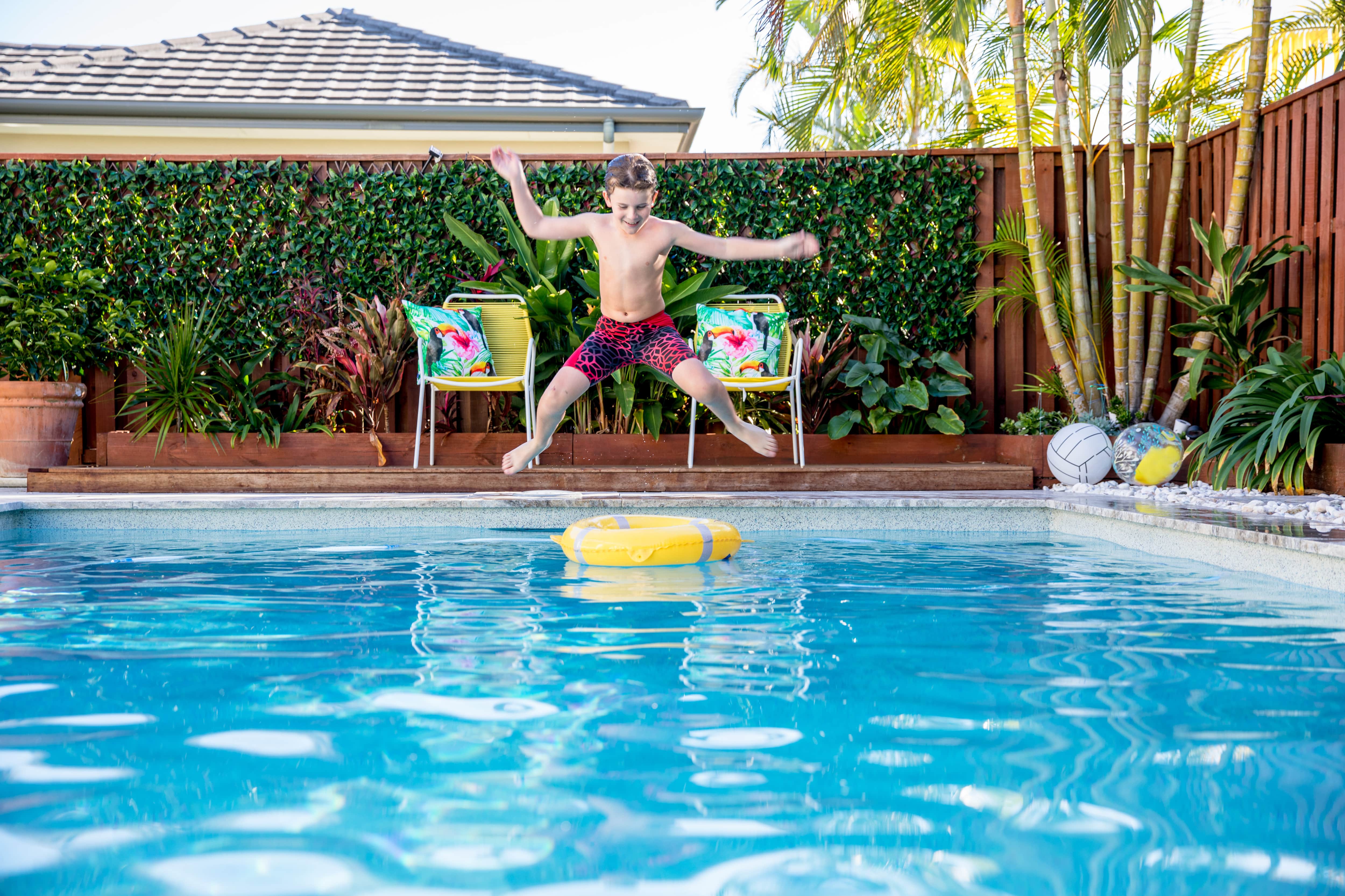  A boy jumps into a pool in front of a wall with vines growing on it