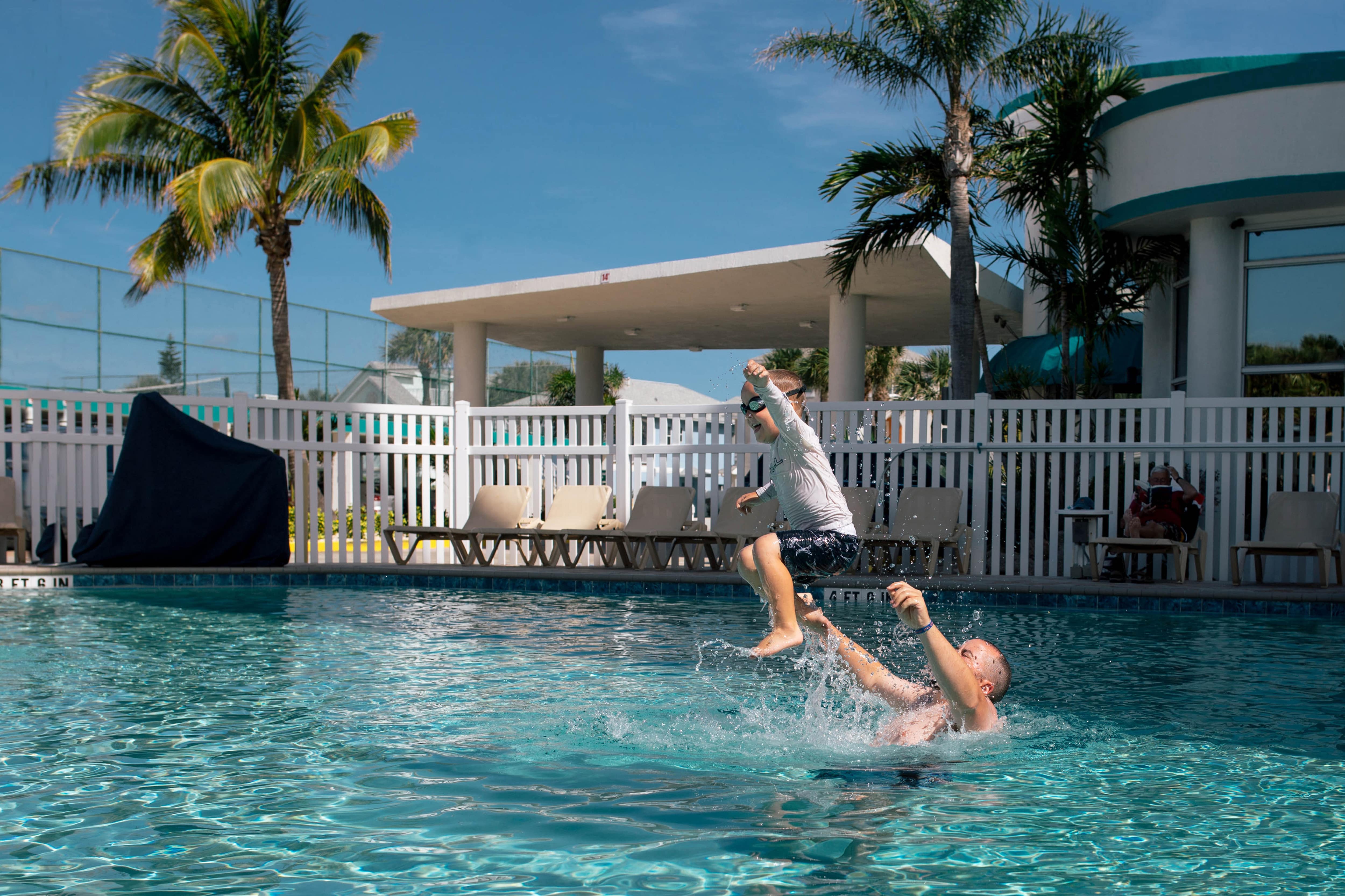 A father and son play in an inground pool fenced off with a vinyl fence