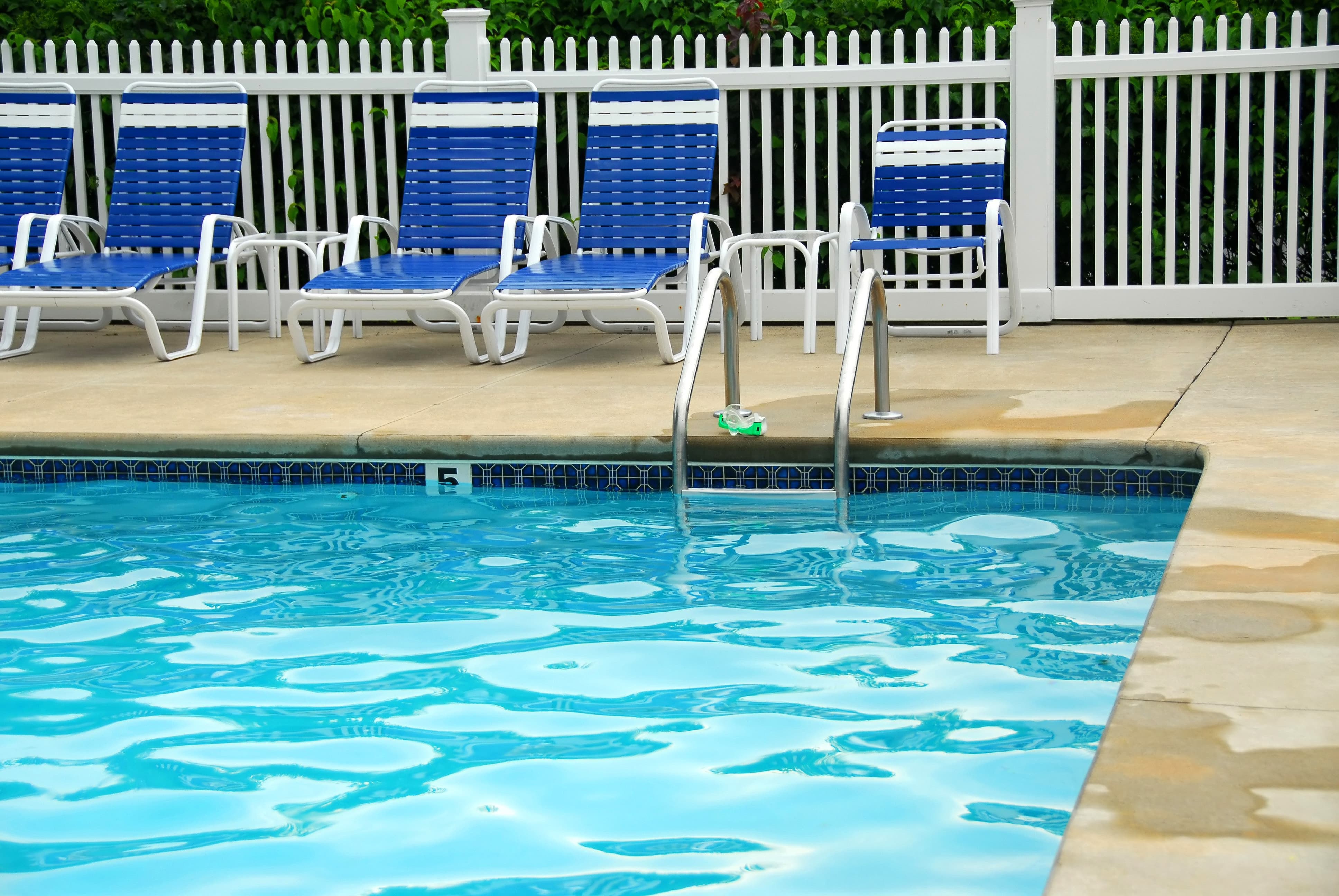 Lounge chairs near a pool with a white picket fence behind them