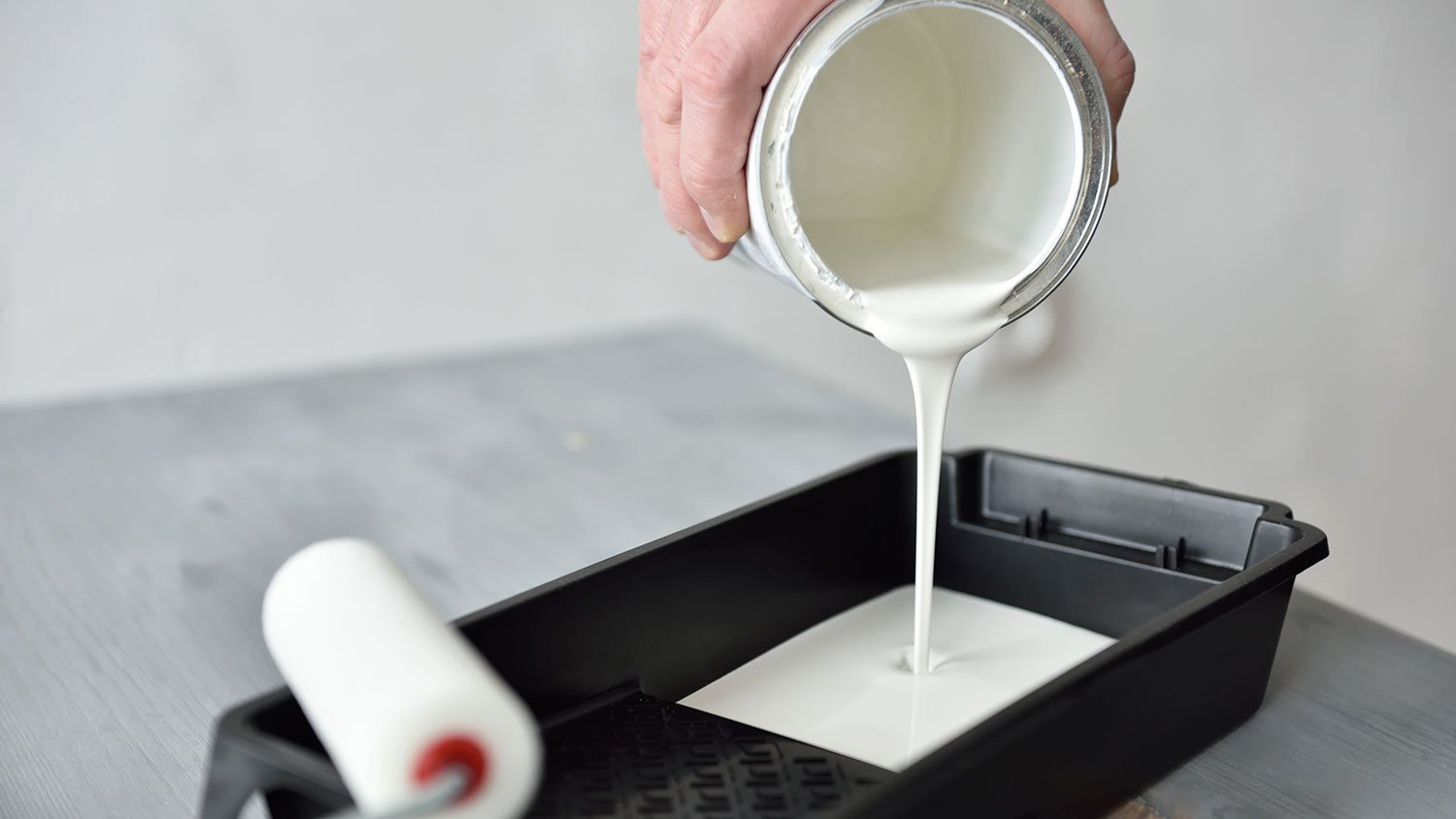 Hand pouring white paint into a painting tray