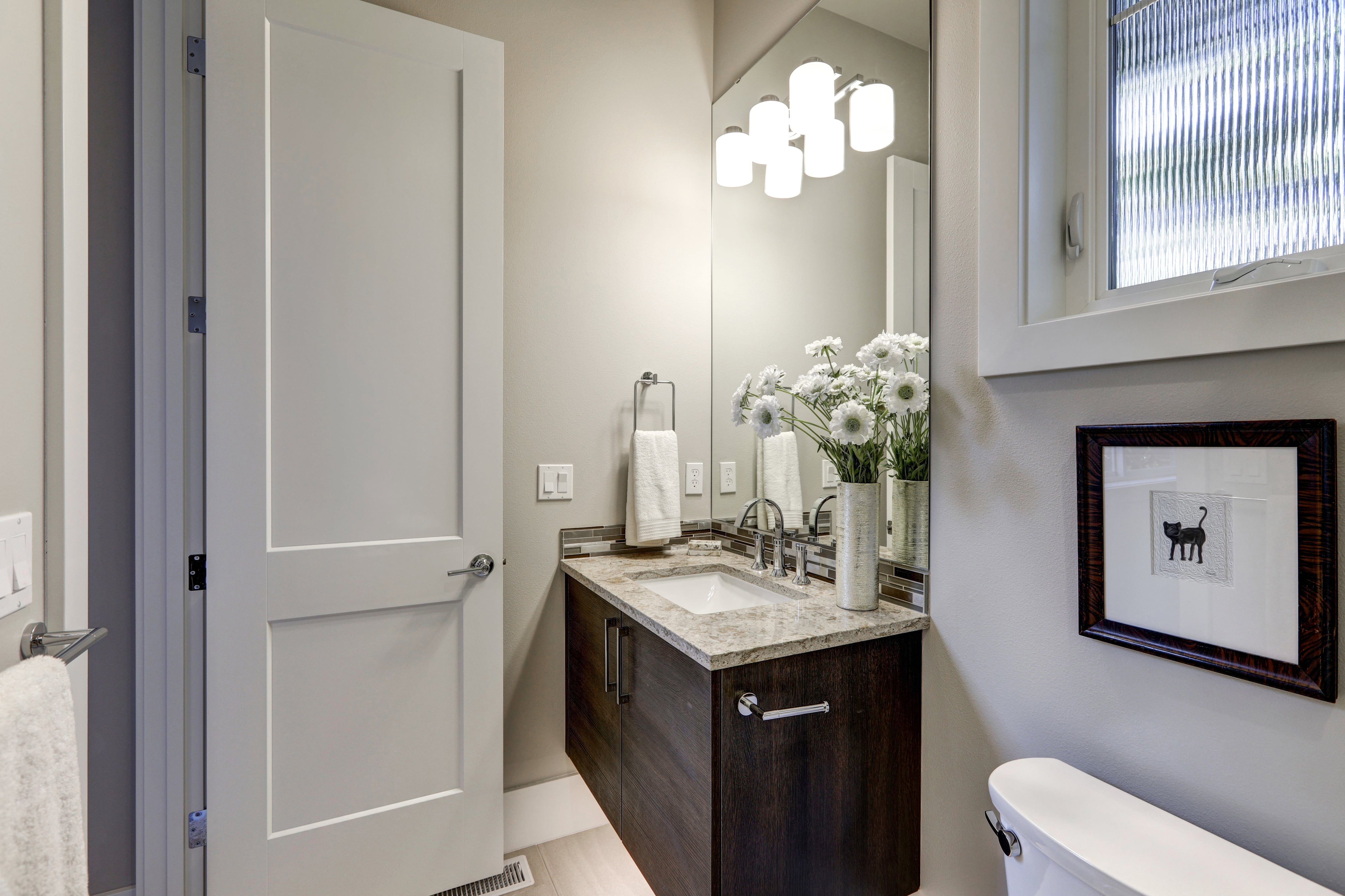 Modern white and gray bathroom with small corner vanity, mirror, and brushed nickel fixtures