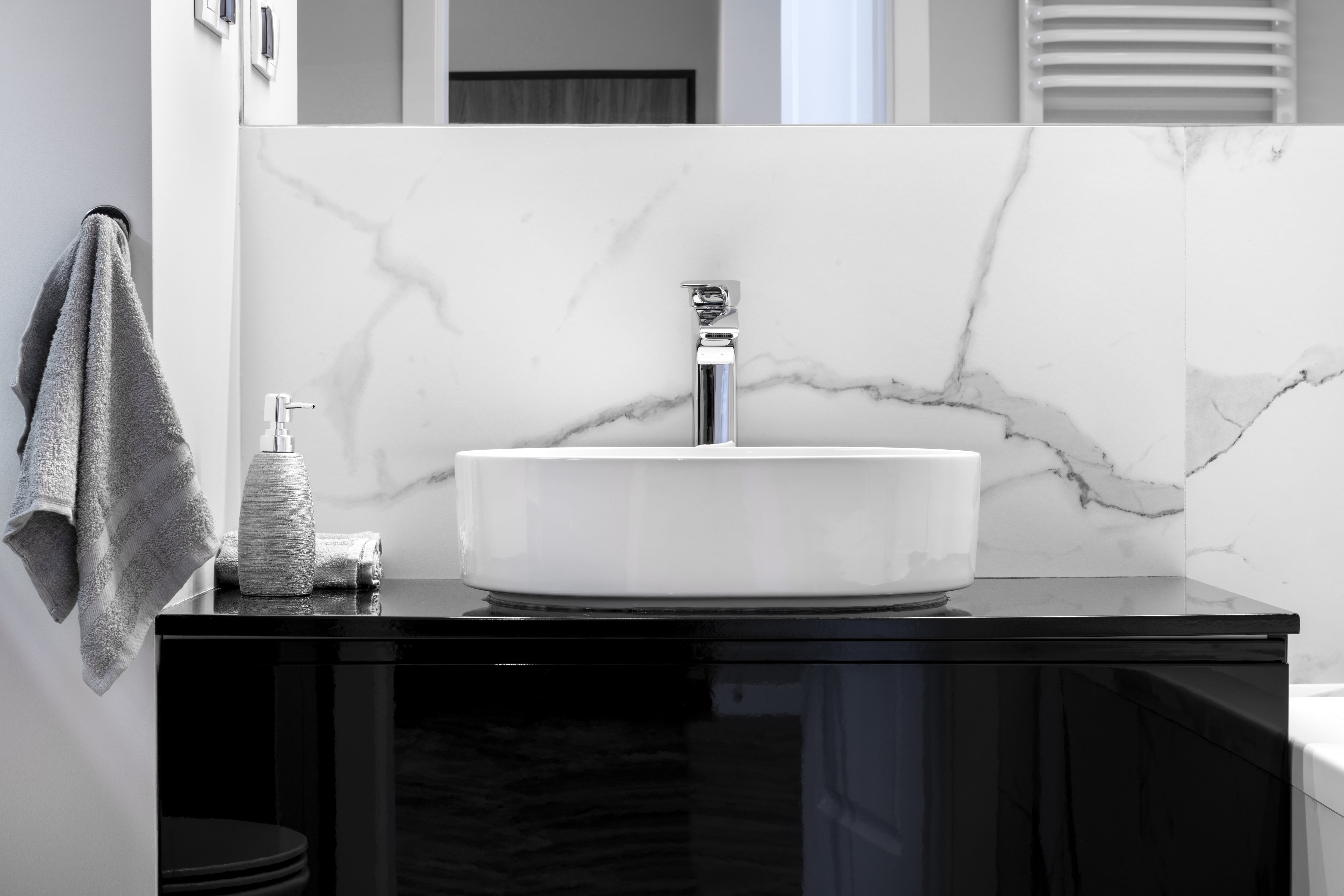 Modern bathroom with white marble walls, a large mirror, black vanity, white sink, and chrome hardware