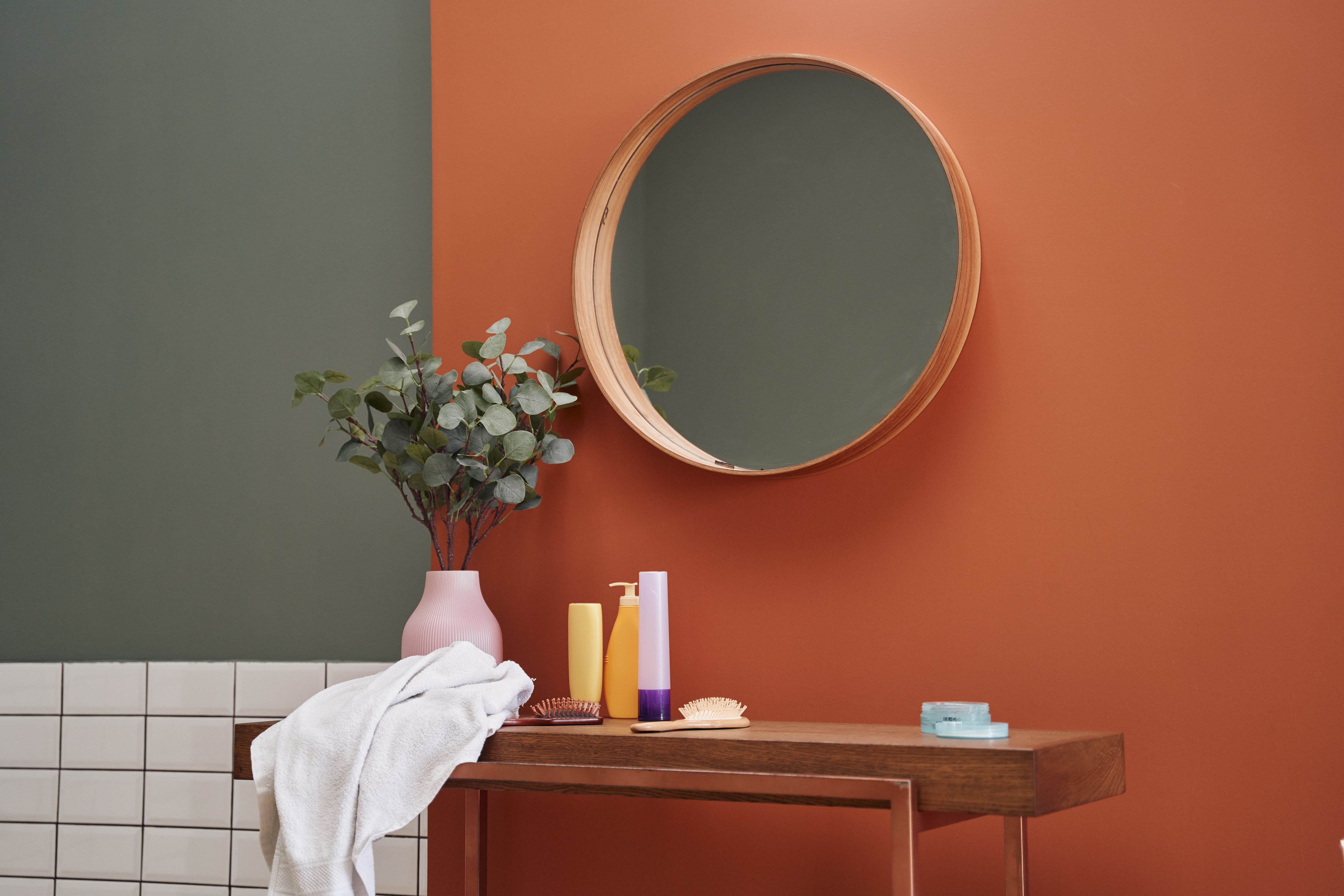 Modern bathroom with orange and green walls, subway tile, a wooden makeup table, and a round mirror