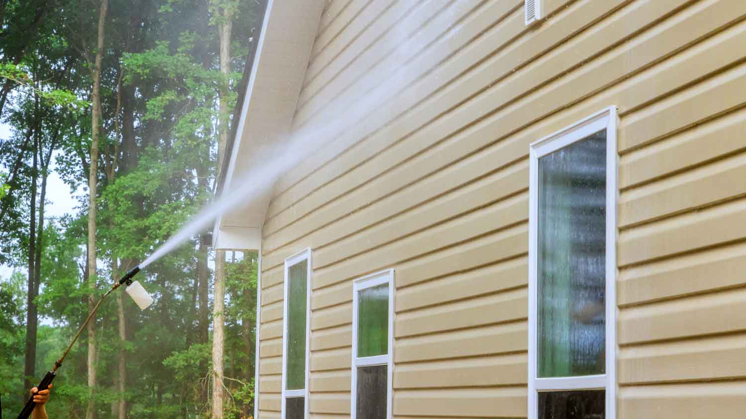 Person using power washer to wash house siding