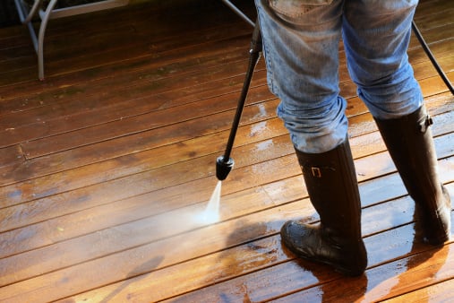 Handyperson using the pressure washer to clean a wooden deck