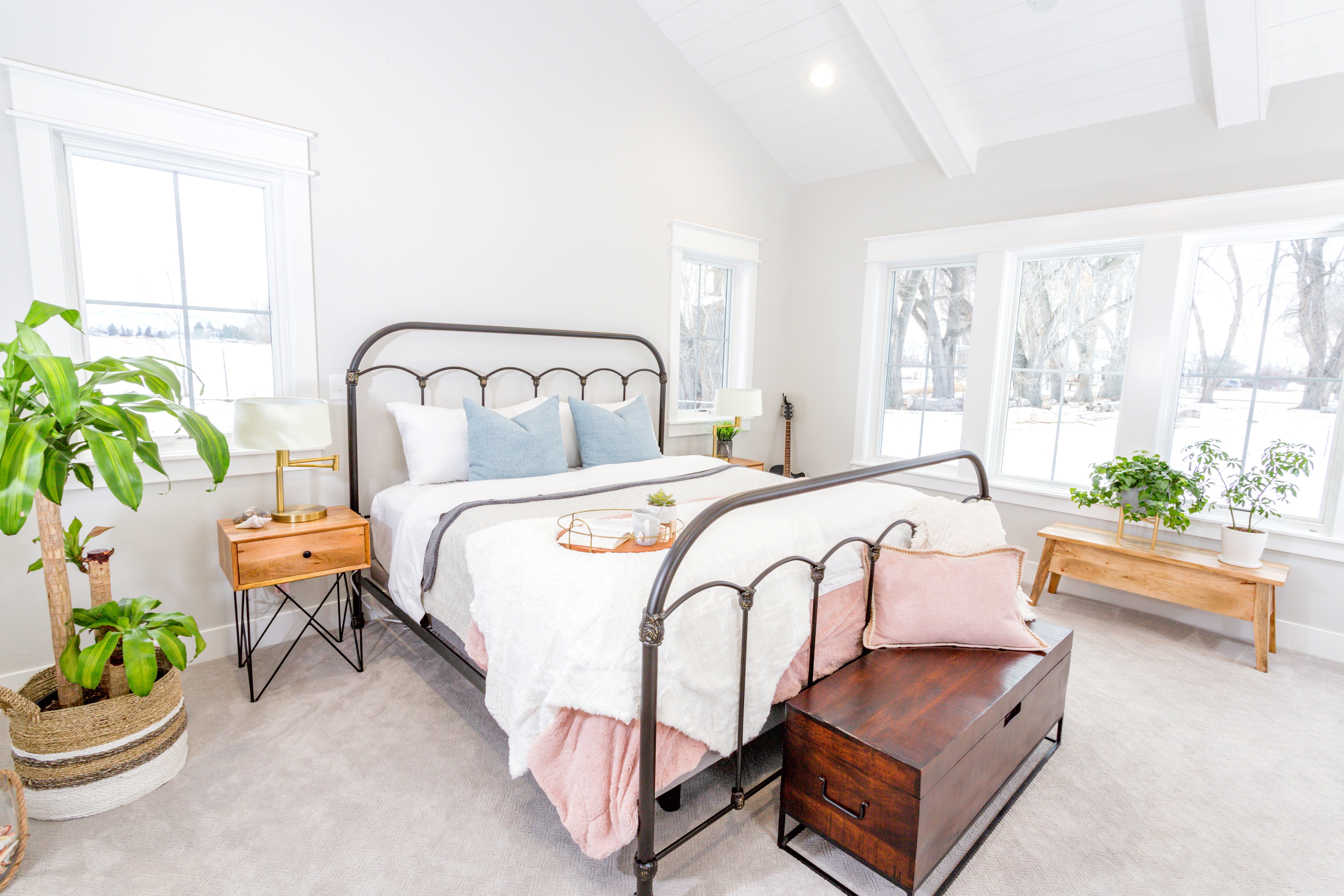 White bedroom with an iron bed, pastel bedding, rustic wood furniture, a shiplap ceiling, and a potted tree