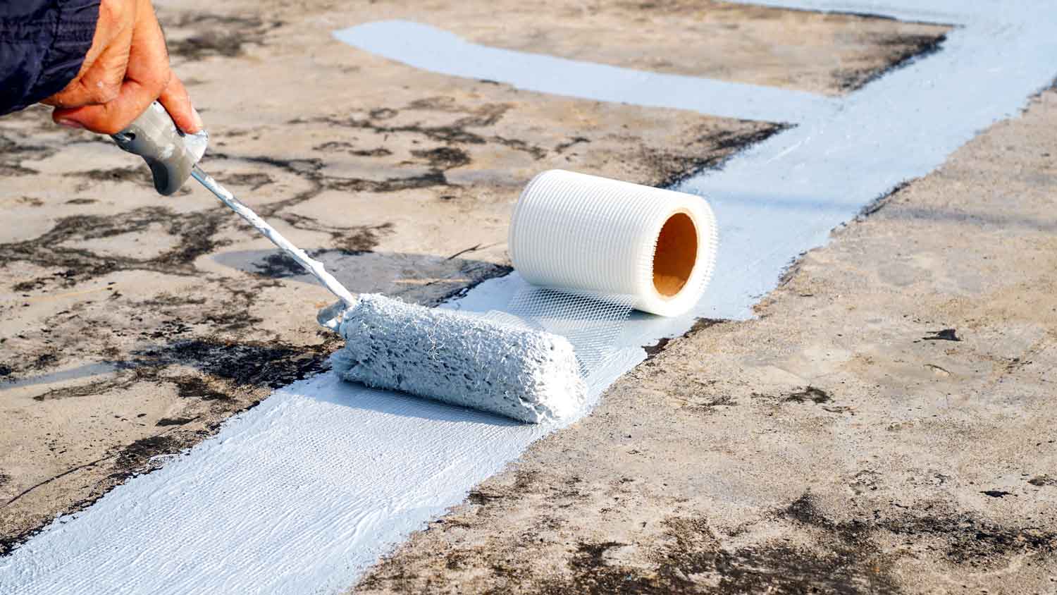 A professional applying primer with a roller on a roof