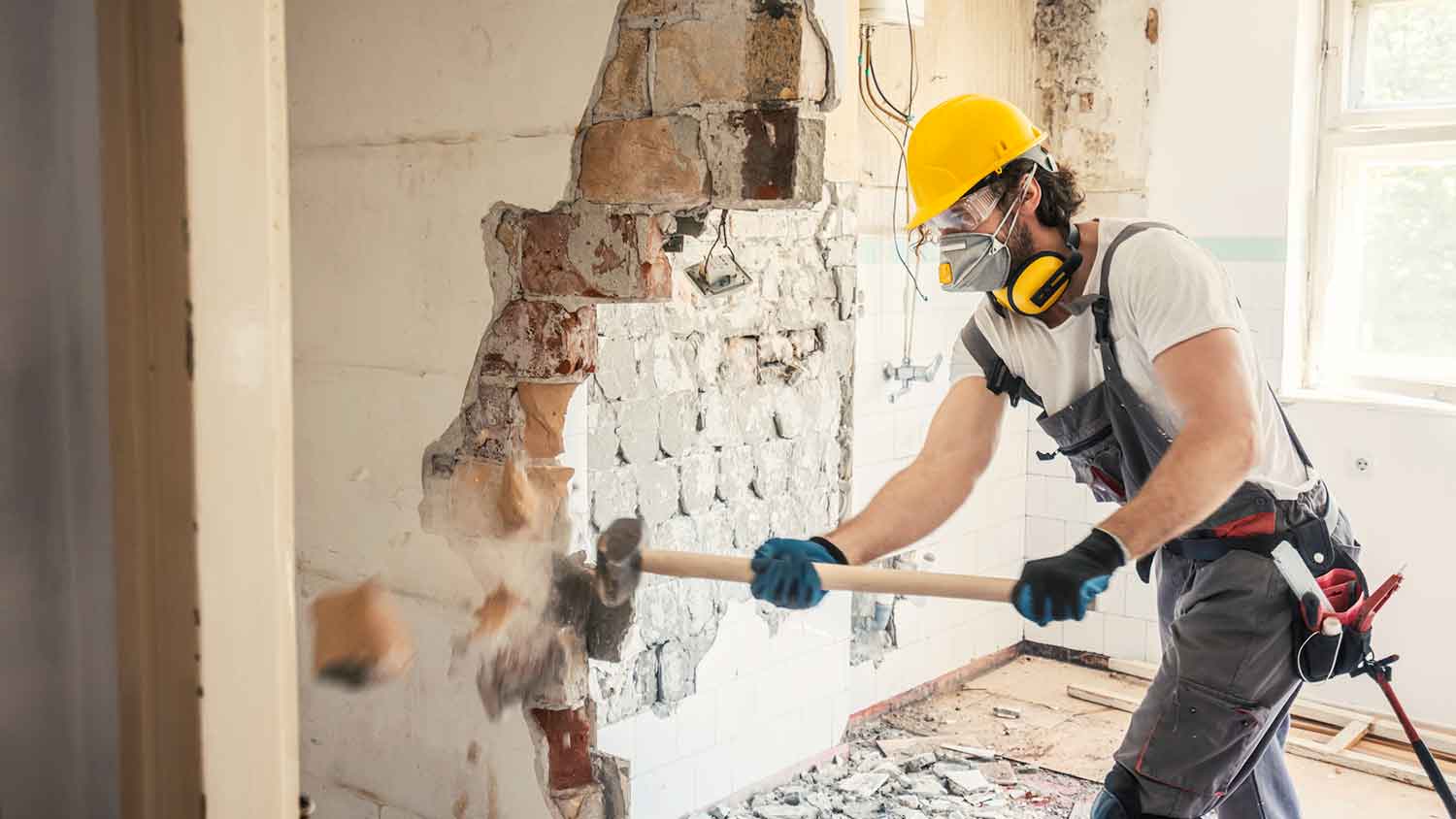 Worker using sledgehammer to demolish interior wall