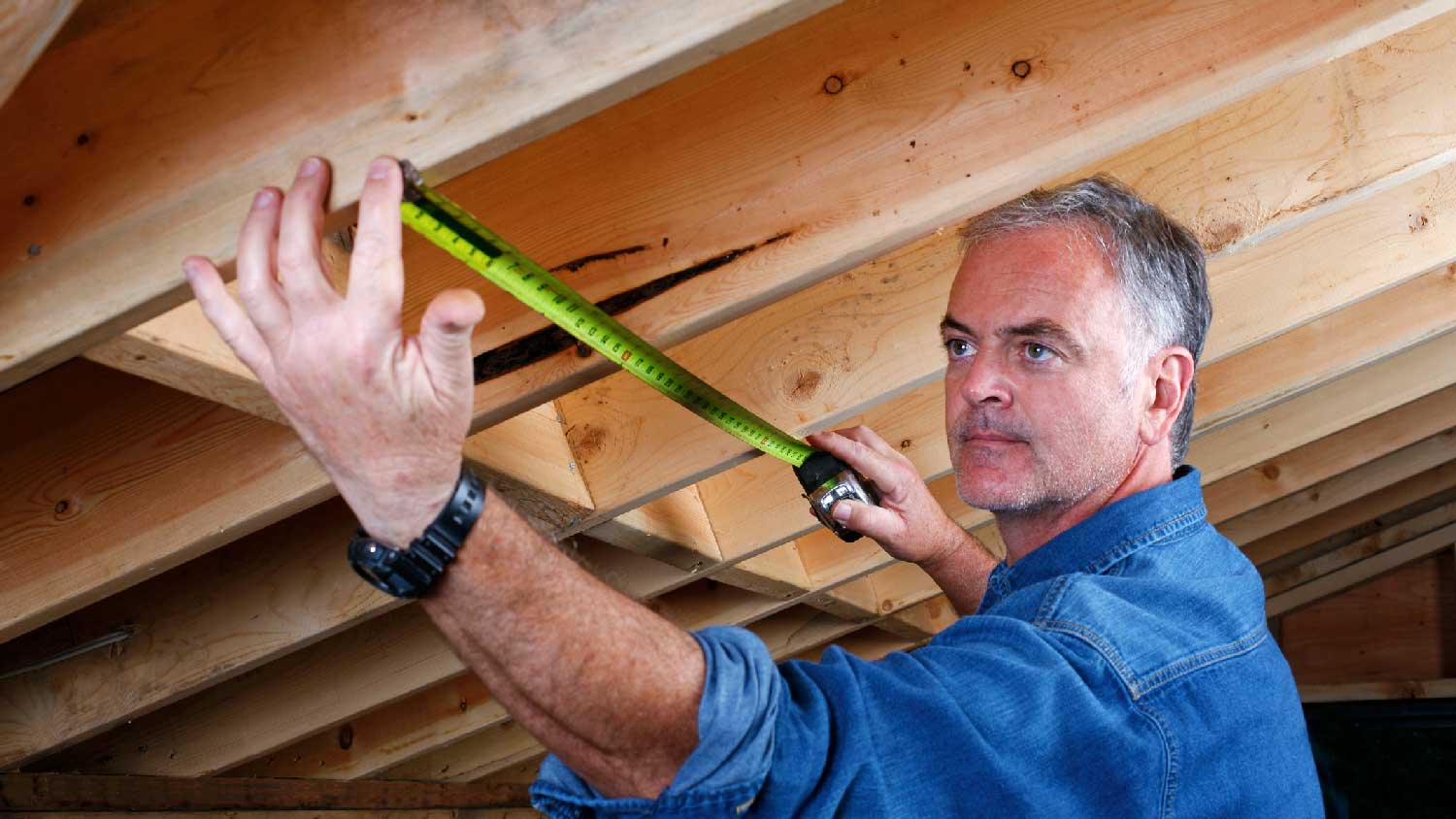 A professional measuring the distance between the roof beams