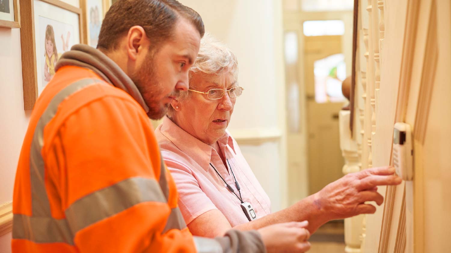 A professional installing a thermostat in an senior woman’s house