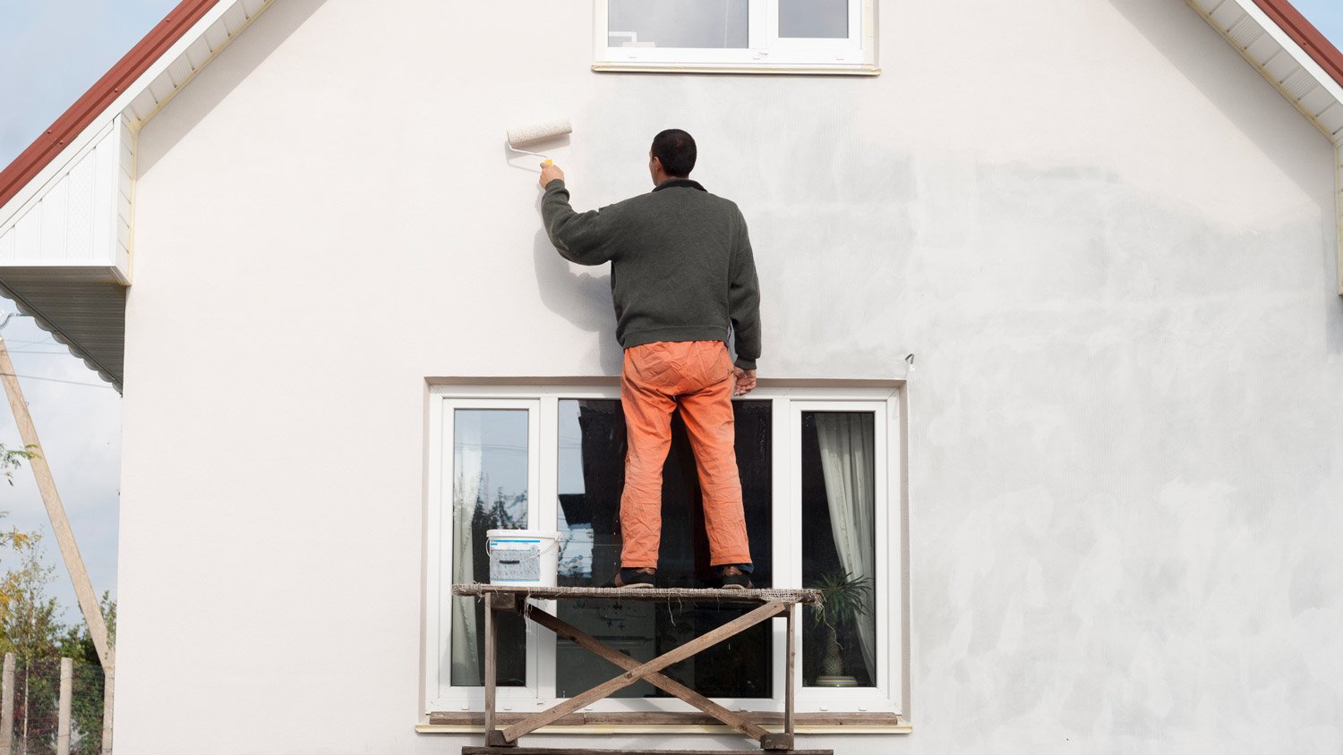 A professional painting the exterior of a house with a roller