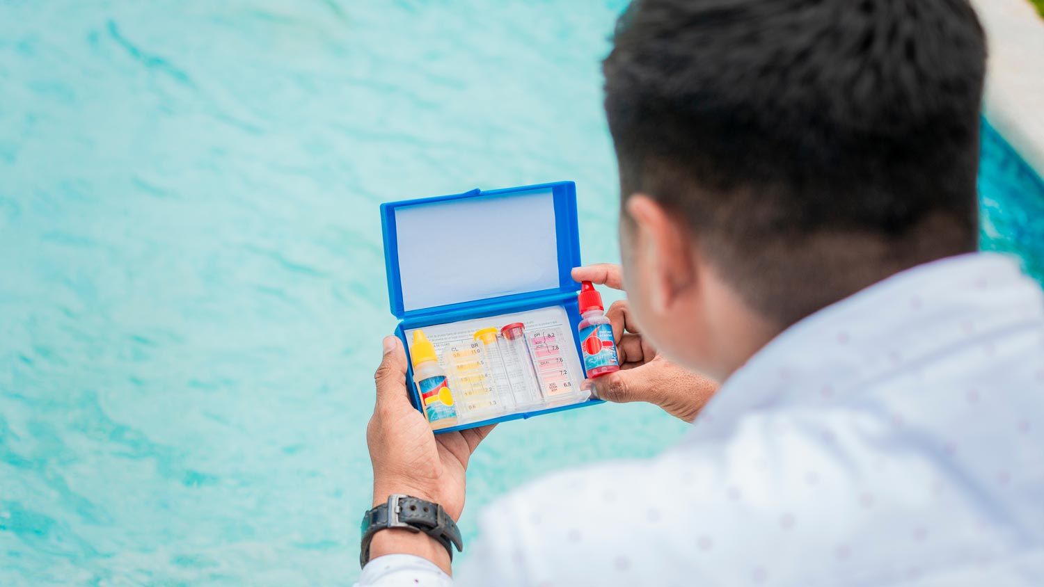 A professional holding a pH test kit in front of a pool