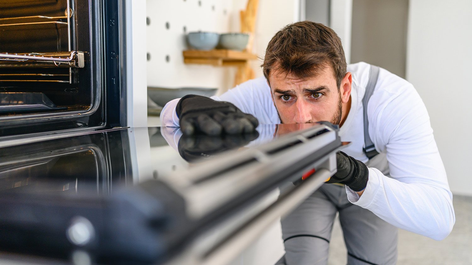 A professional repairing an oven in a kitchen