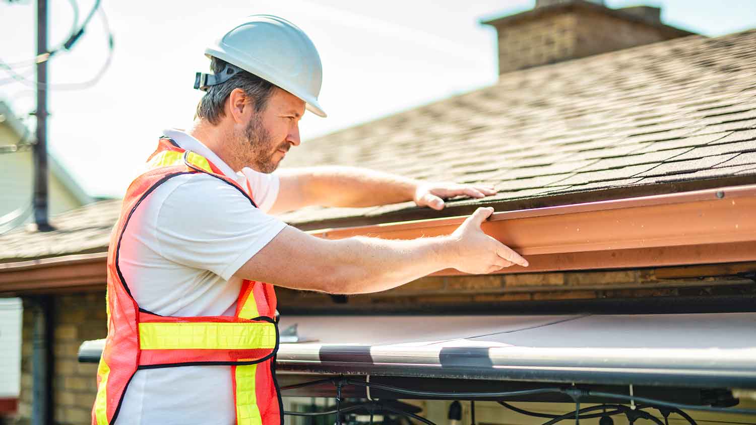 Contractor wearing a helmet inspecting roof gutters