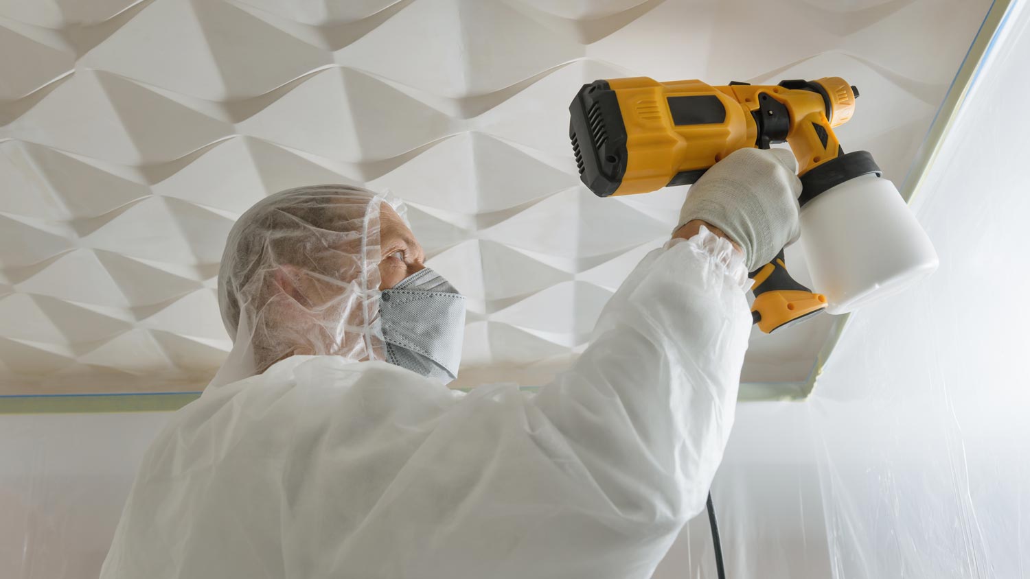 A man spraypainting a textured ceiling