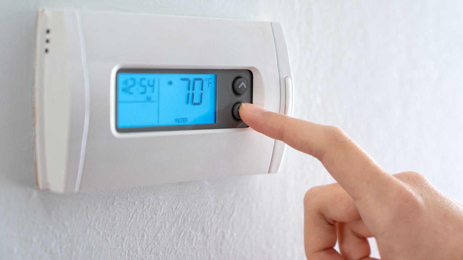 person pushing digital thermostat 