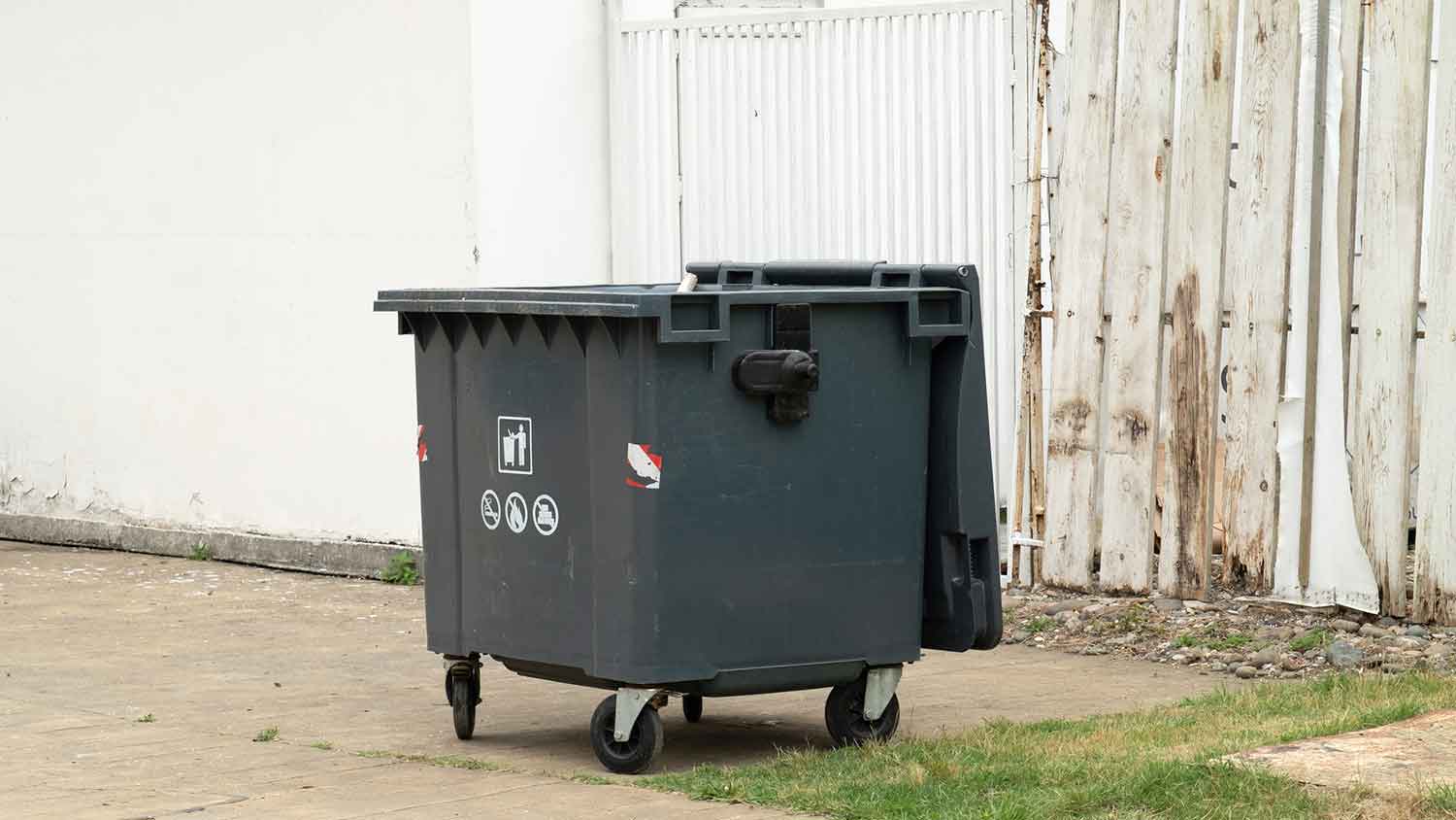 Real load dumpster sitting outside of a white building 