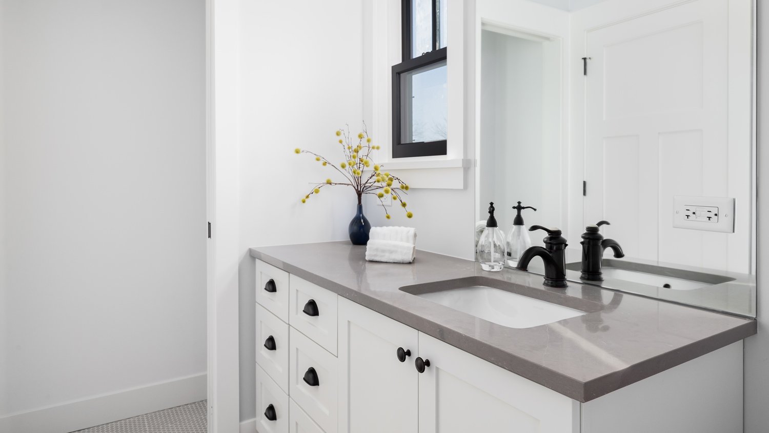 A bathroom with a white cabinet, grey granite countertop, and black faucet