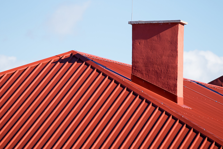 closeup of red metal roof with chimney against blue sky background