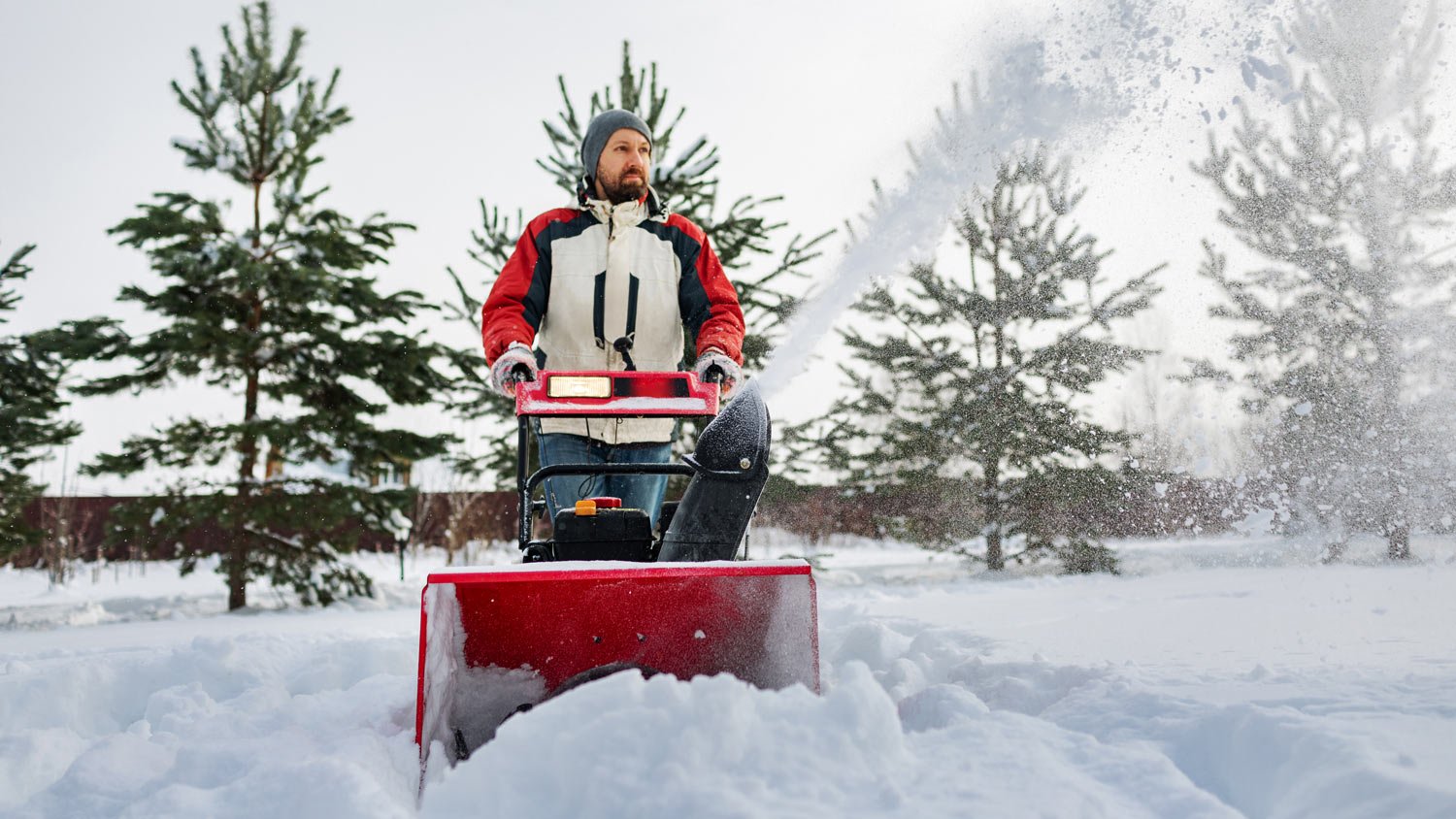 Adult man removing snow with snowblower at heavy snowfall