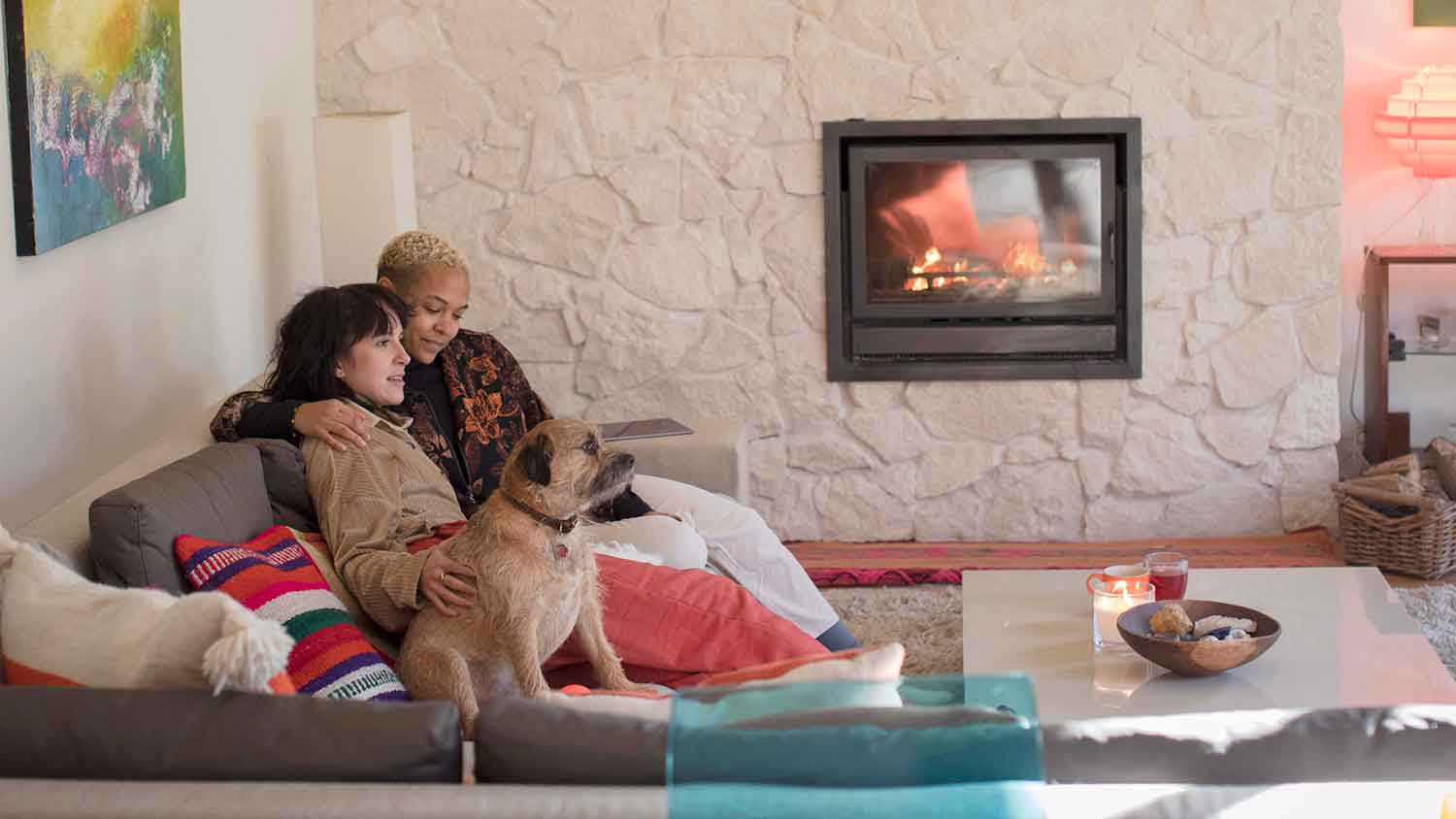 A couple sitting on the sofa with their dog and enjoying the fireplace