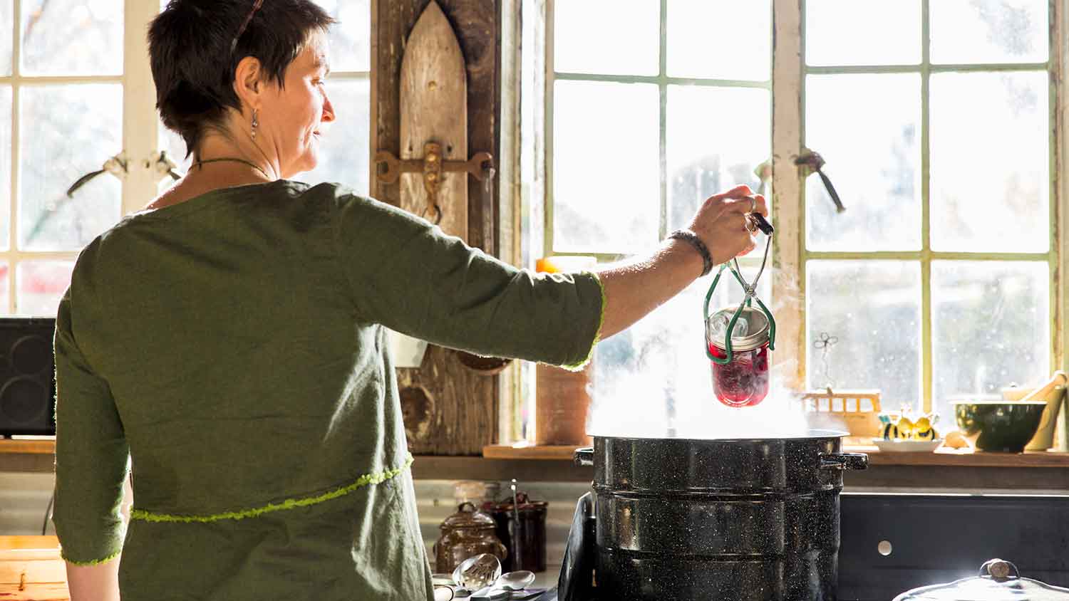 Woman removing pickling jar from steaming pot