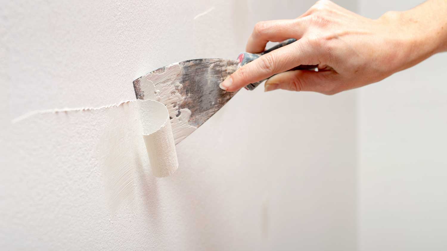 Handyperson using a wall scraper to remove texture from a wall