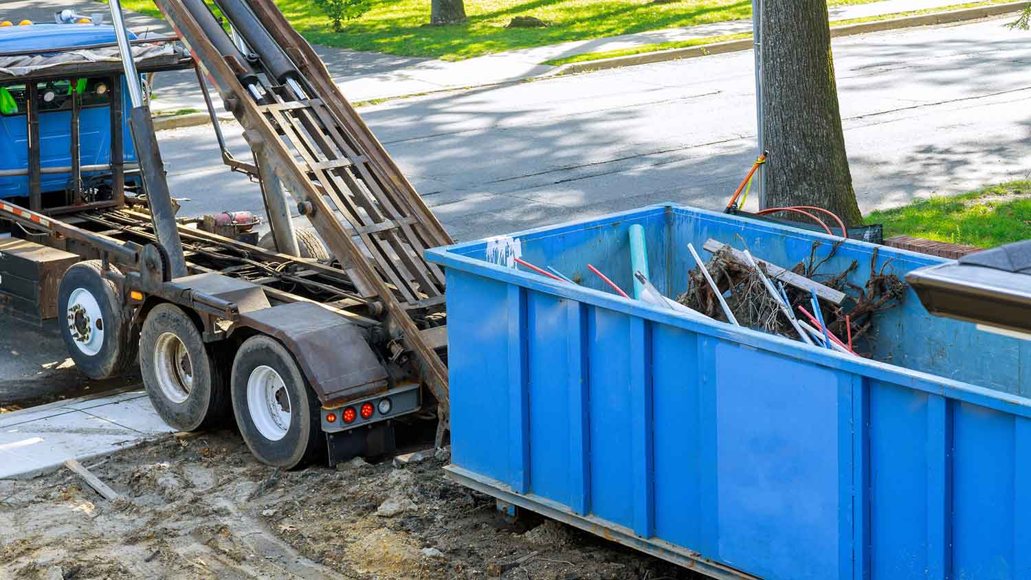 Flatbed truck removing roll-of dumpster from a property
