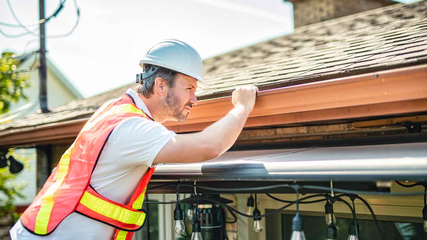 Roofer wearing a helmet inspecting roof shingles 