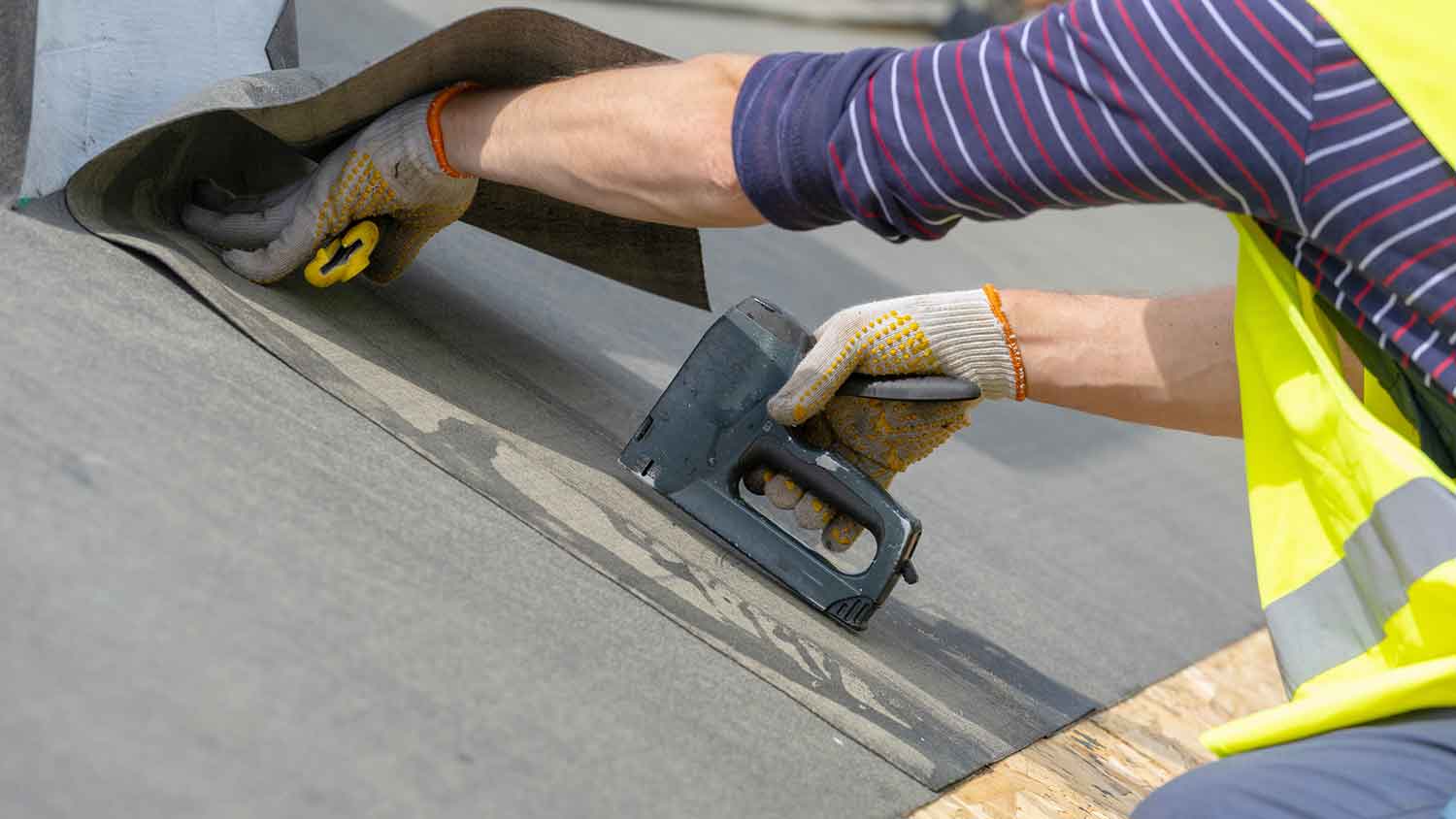 Worker using stapler to install roof underlayment