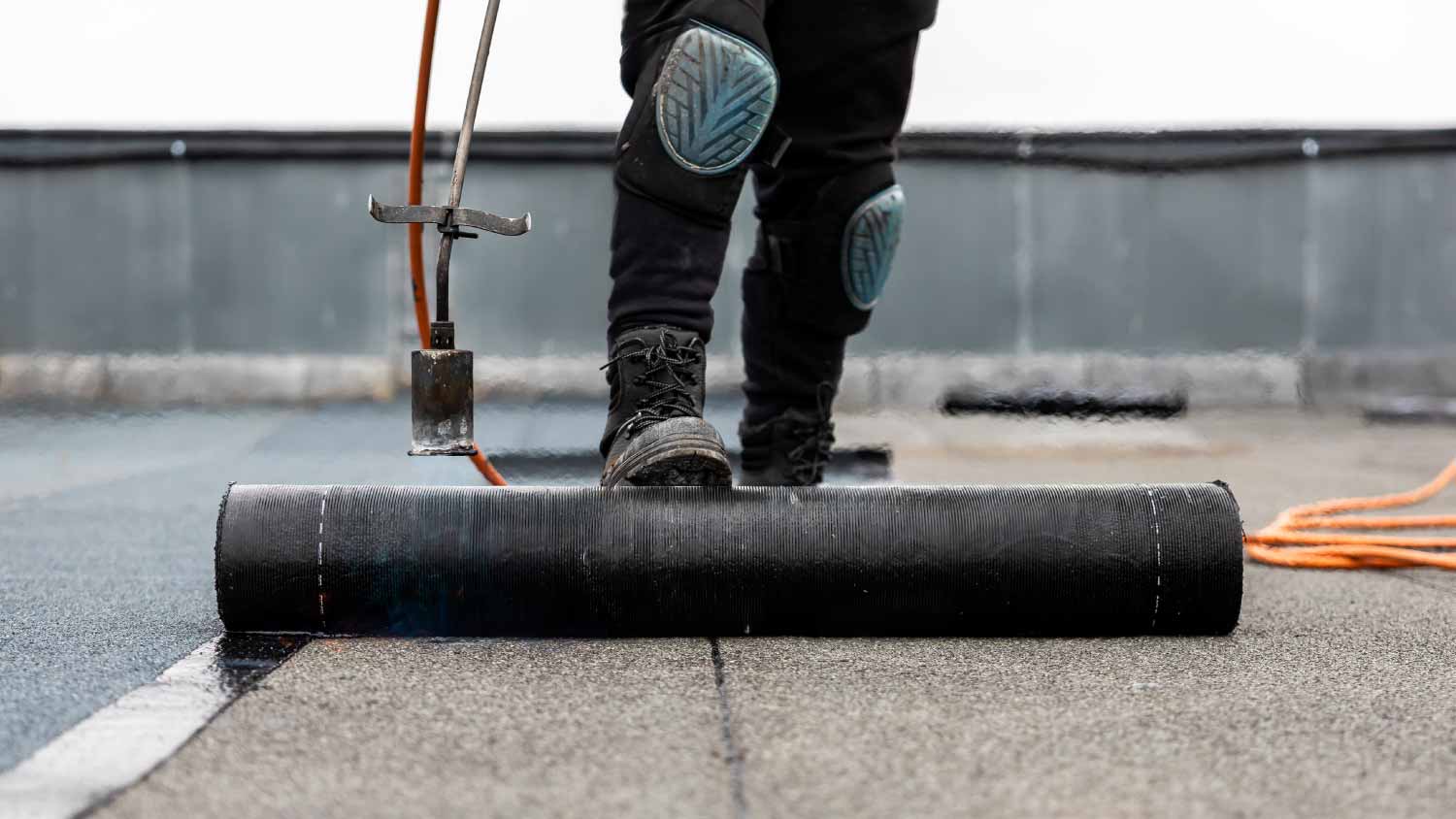 Roofer applying bitumen roll on flat roof