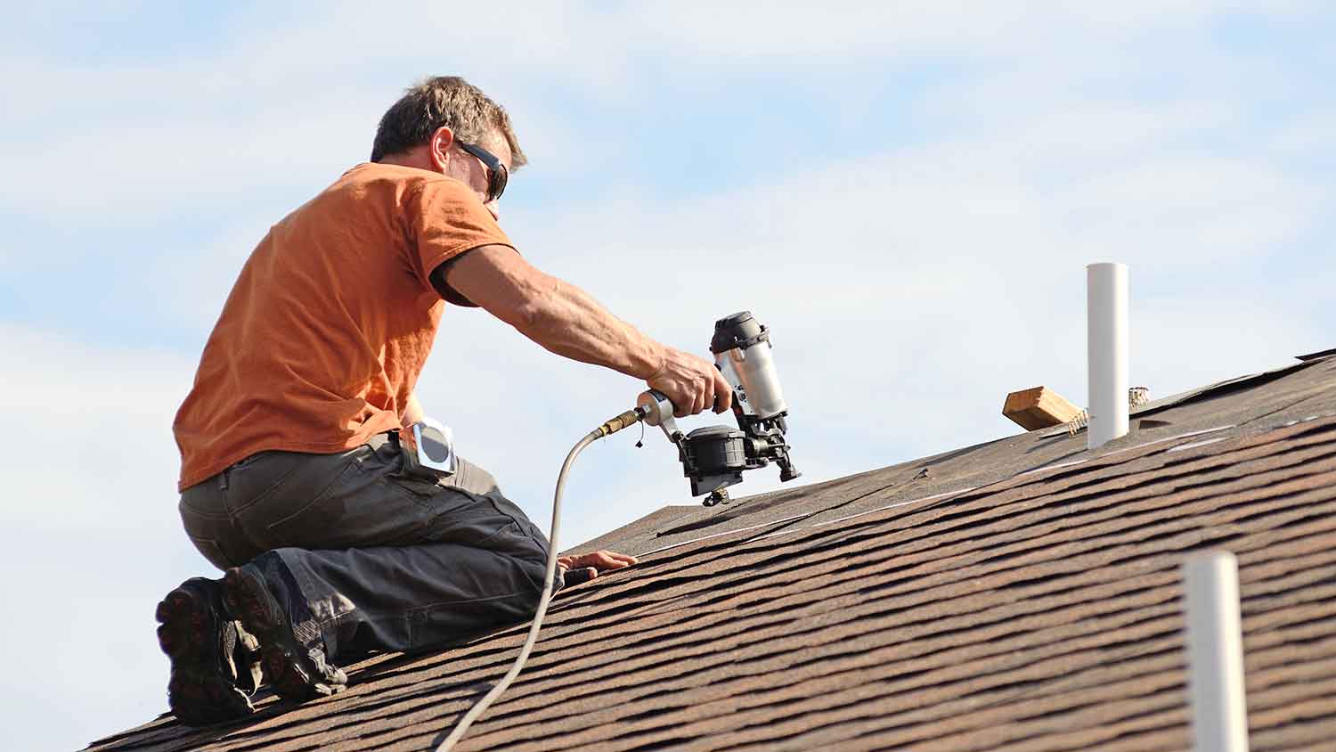 Roofer using nail gun to install asphalt shingles