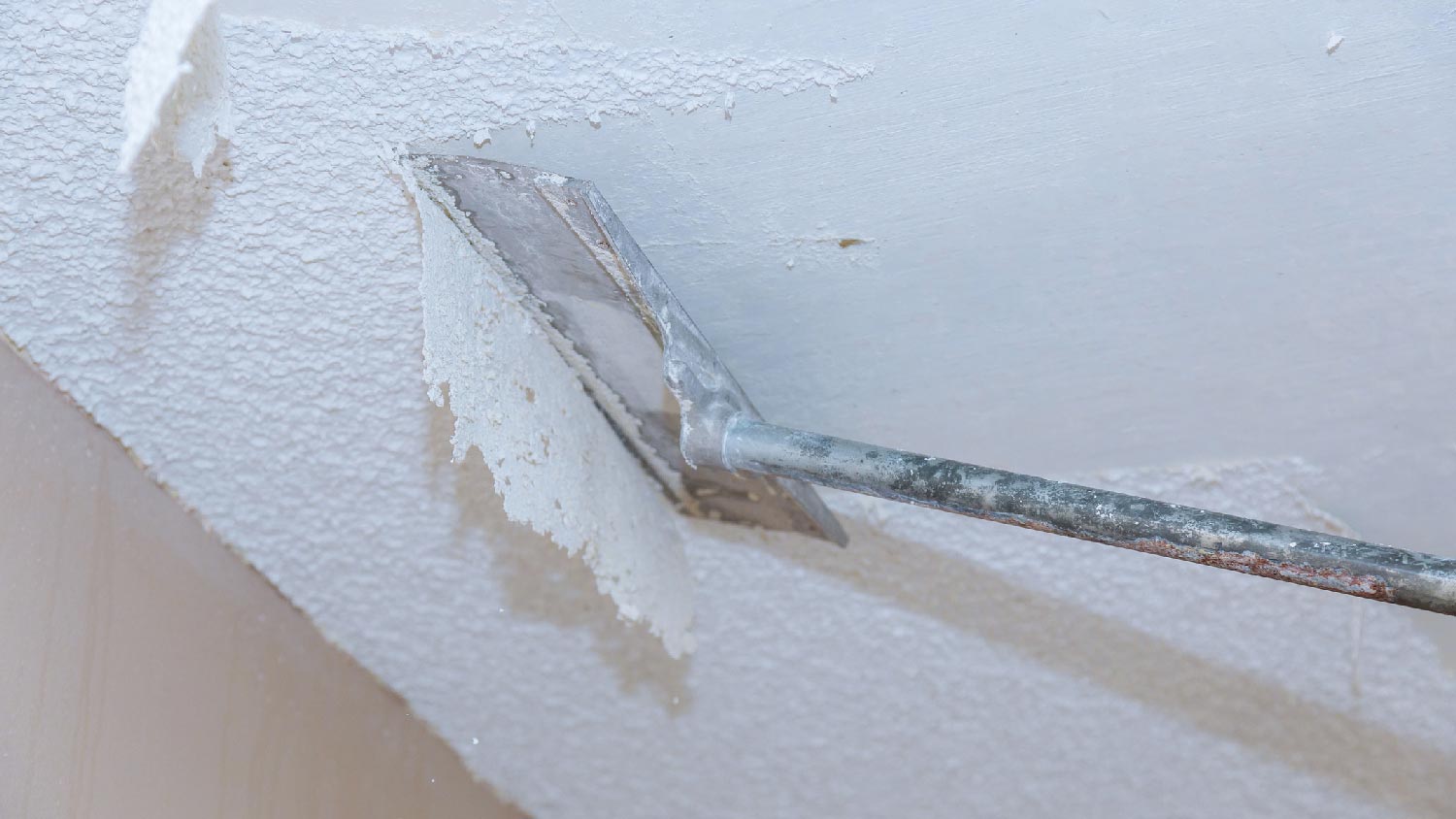 A person scraping off popcorn ceiling