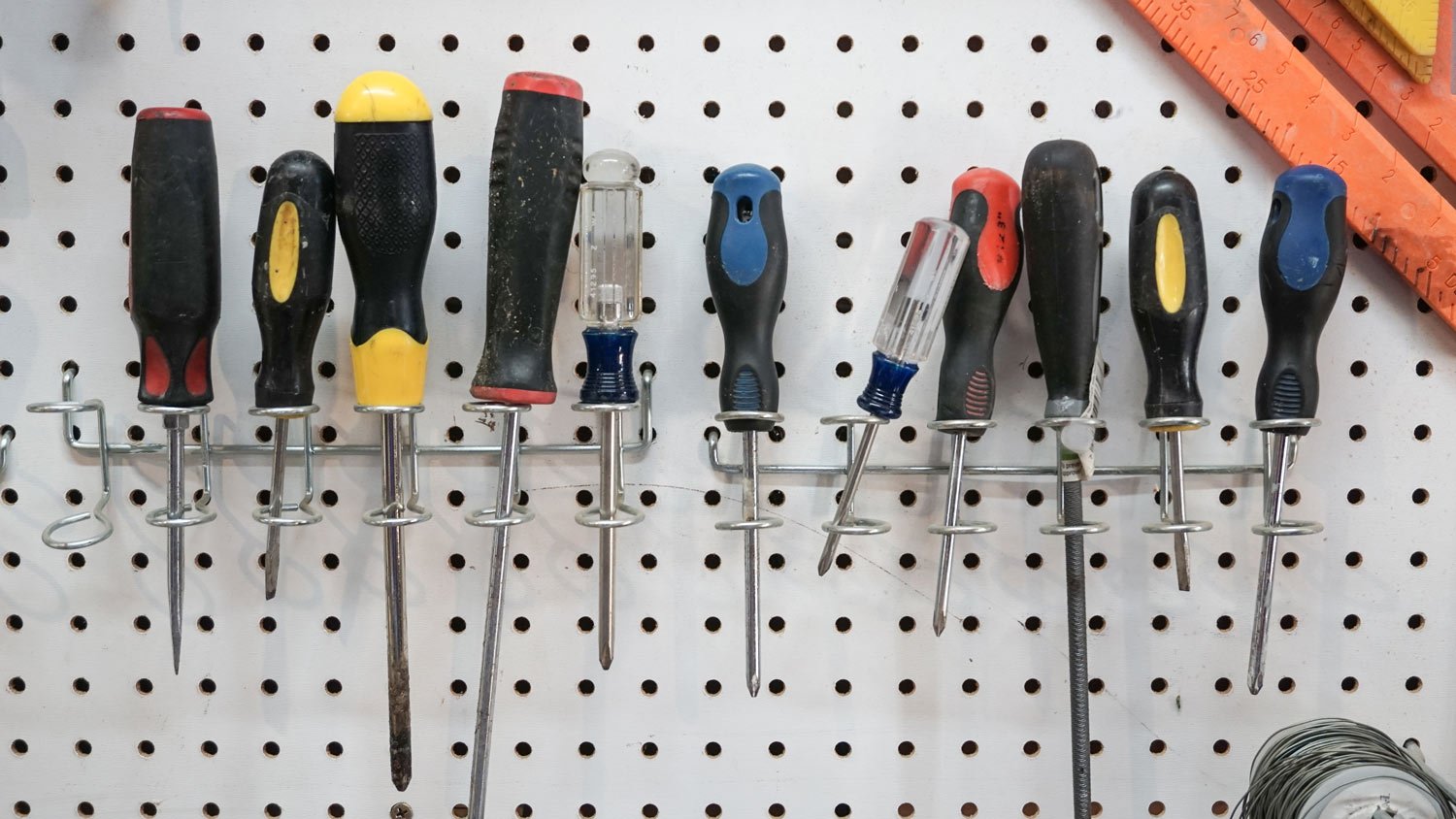 A closeup of screwdrivers hanging from a pegboard in a garage