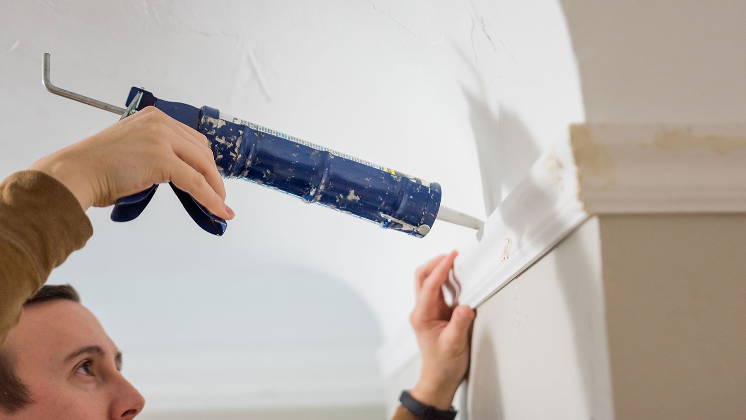 Man holding a caulk gun is sealing wall crack