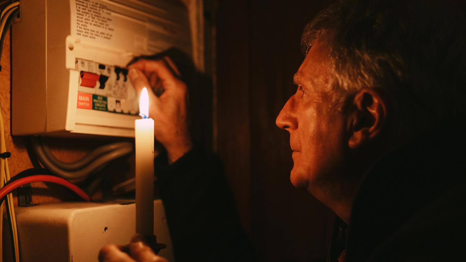 A senior man holding a candle checking the fuse box