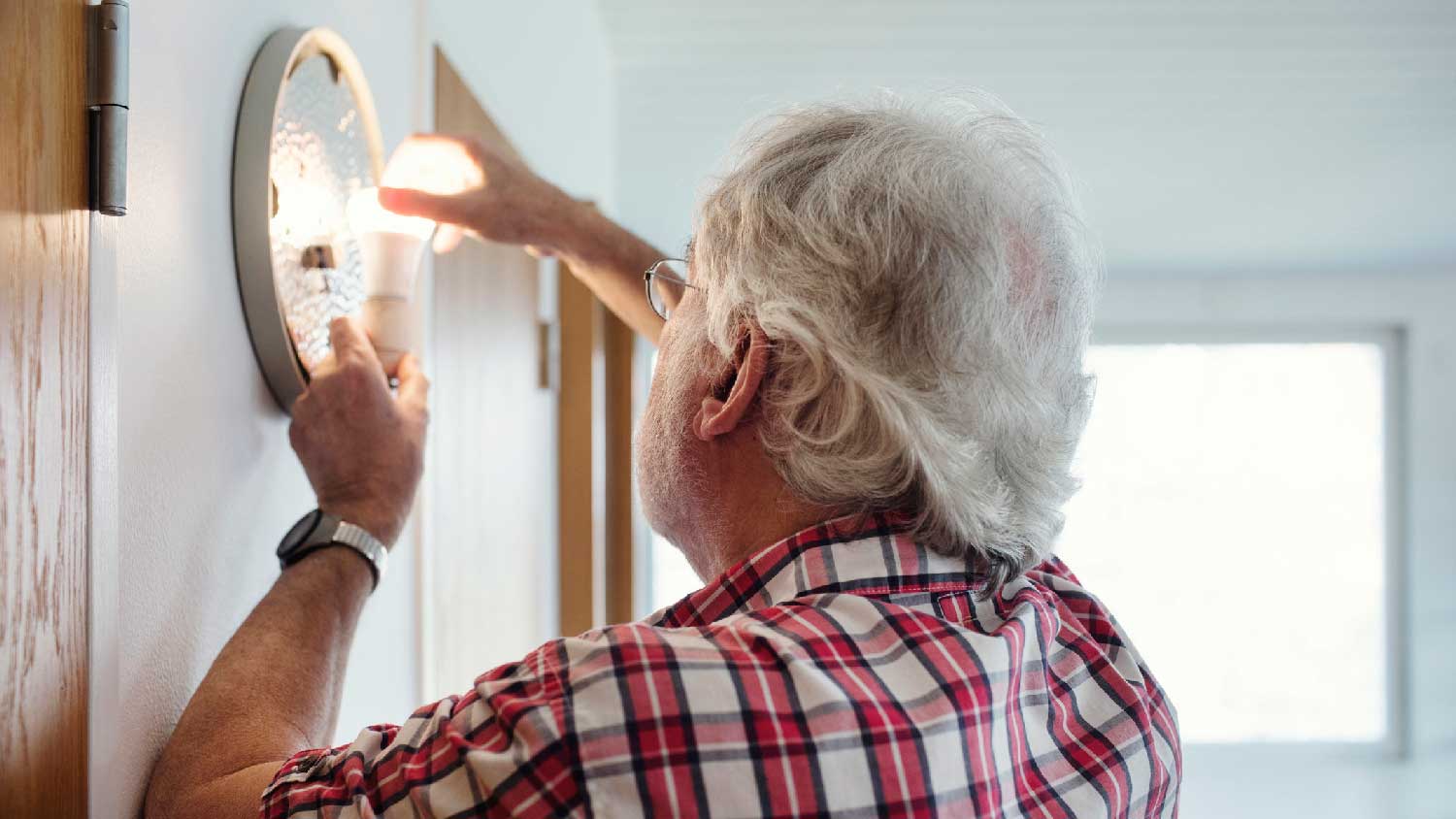 A senior man installing a new bulb in a sconce