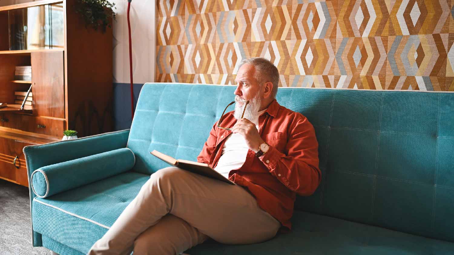 A senior man reading in a room with wallpaper