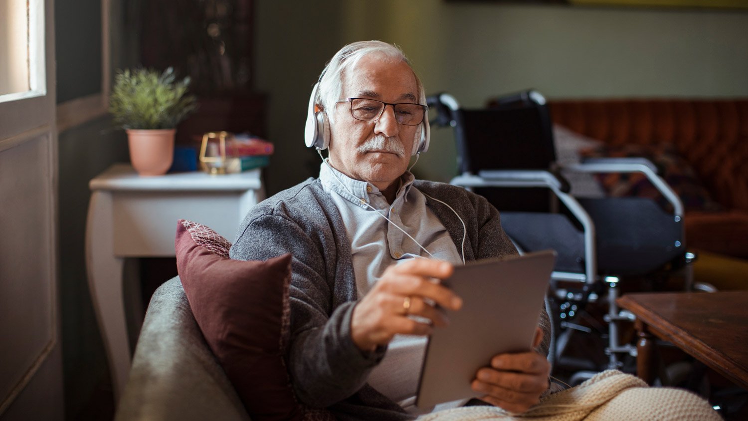 A senior man using a table and headphones on his couch