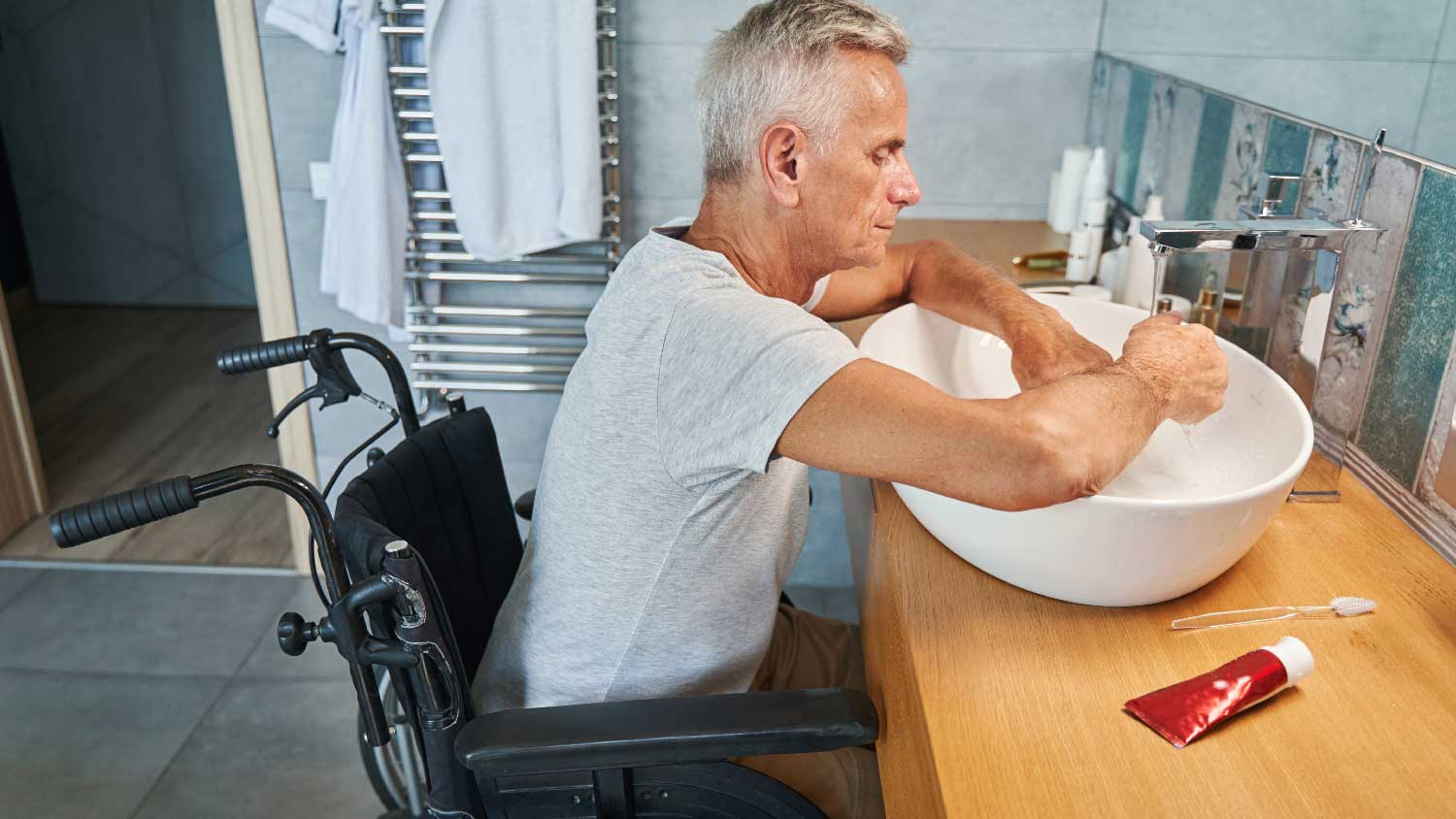 A senior man on a wheelchair washing his hands in a bathroom sink